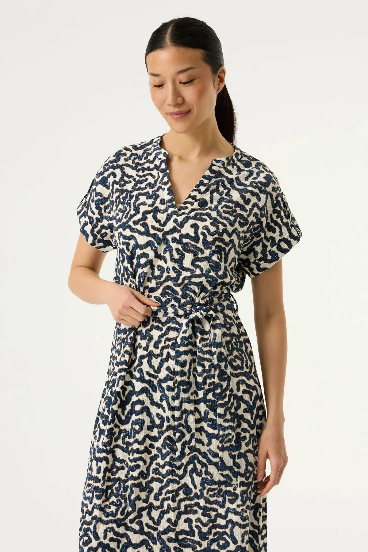 Woman  wearing a textured cream-coloured dress with a dark navy blue abstract wavy pattern and a matching tie belt at the waist.