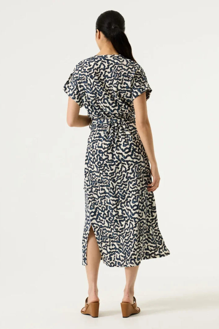 Woman shown from the back wearing a textured cream-coloured dress with a dark navy blue abstract wavy pattern and a matching tie belt at the waist.