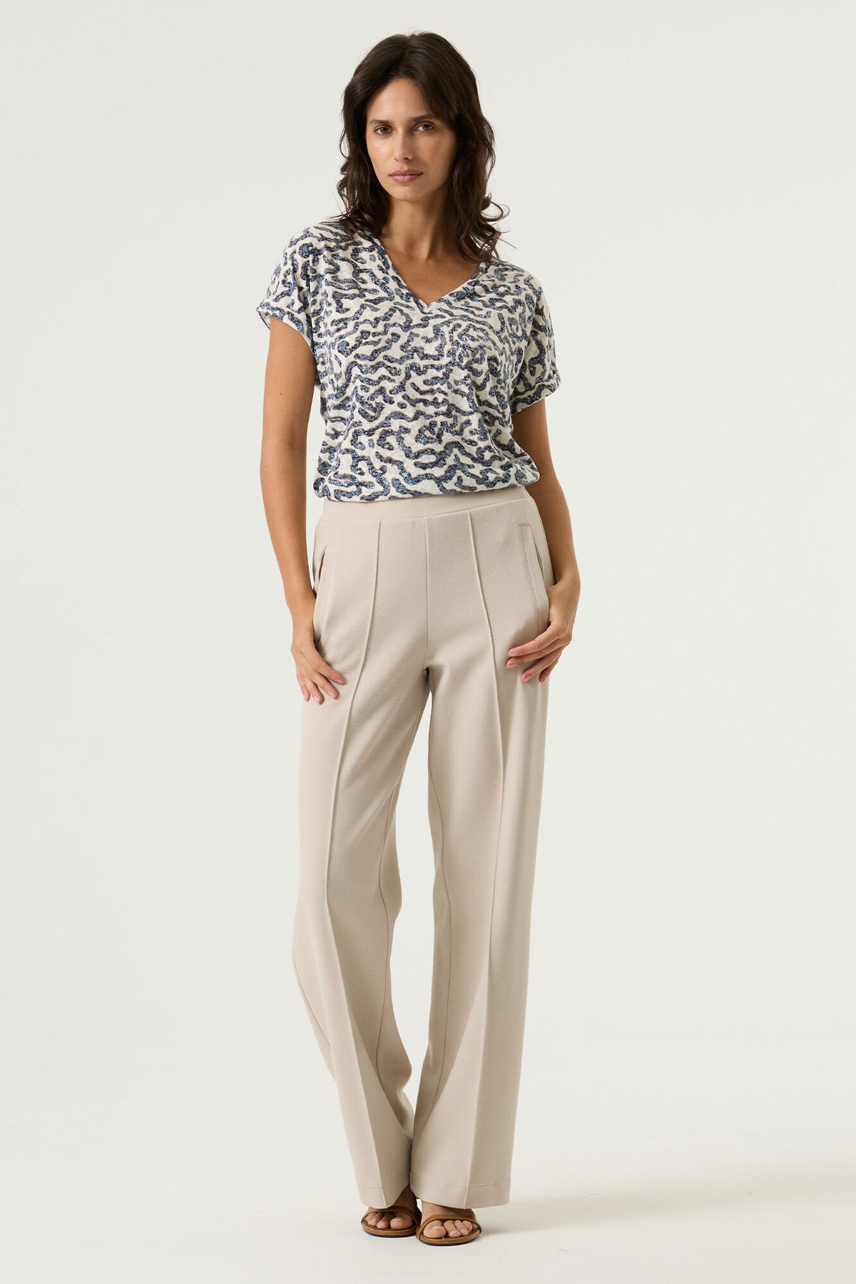 woman wearing a white v neck t-shirt with blue pattern  and cream pants on a plain background
