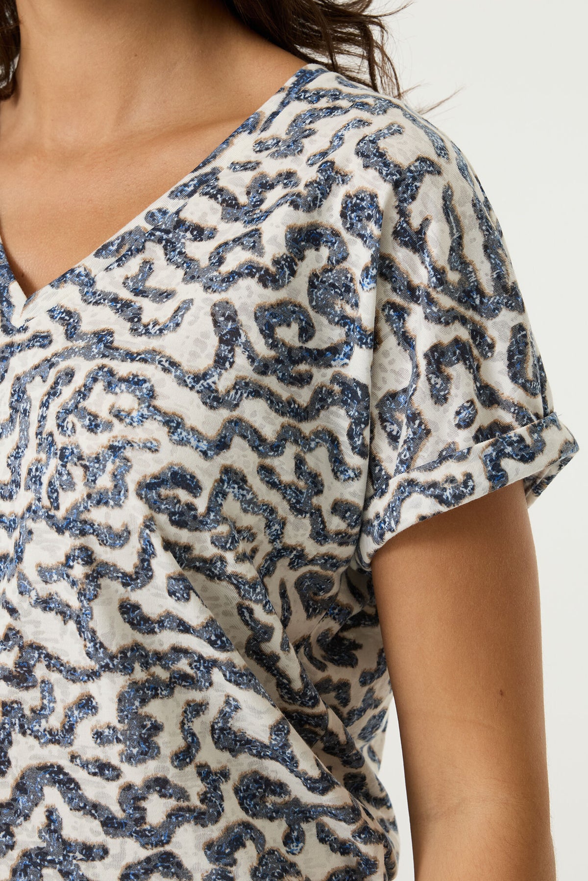 Close-up of a person wearing a white v neck t-shirt with blue pattern on a plain background