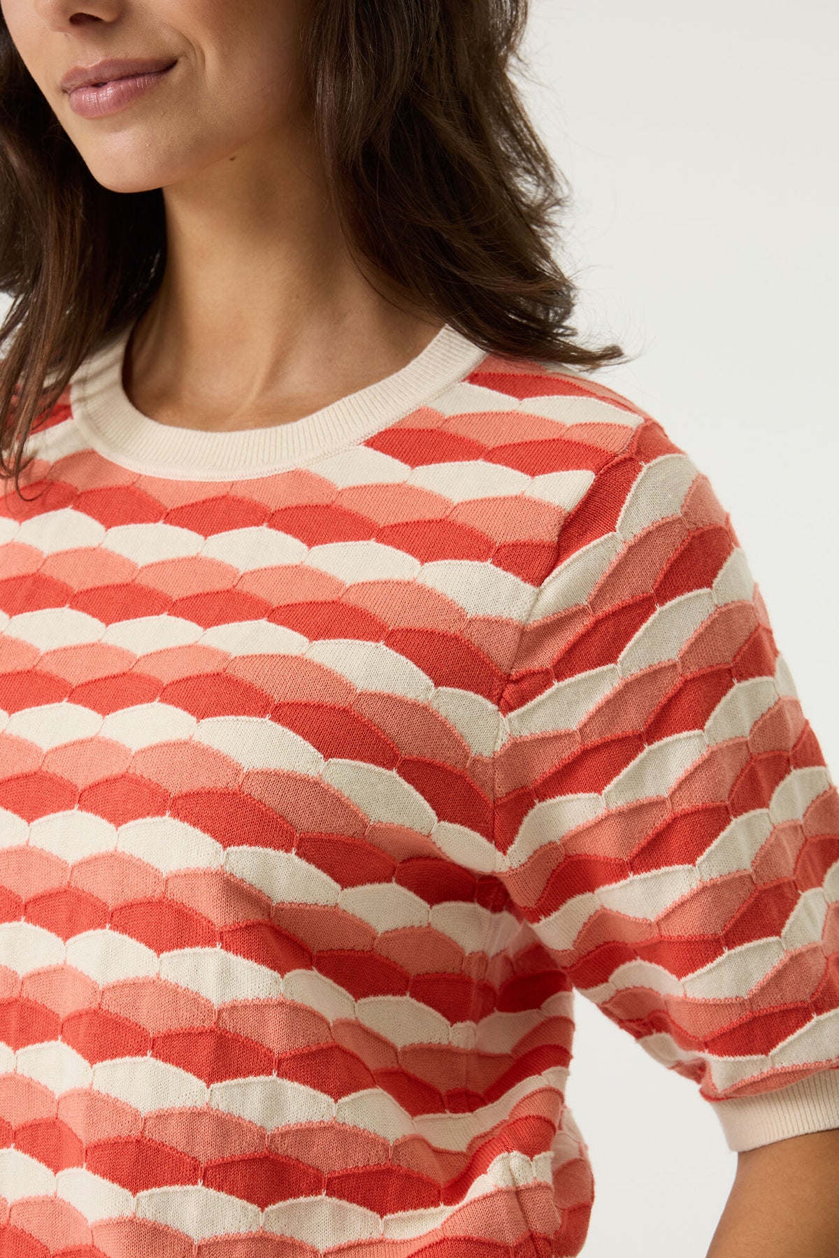 Woman wearing a red and white patterned short sleeve sweater on a plain background