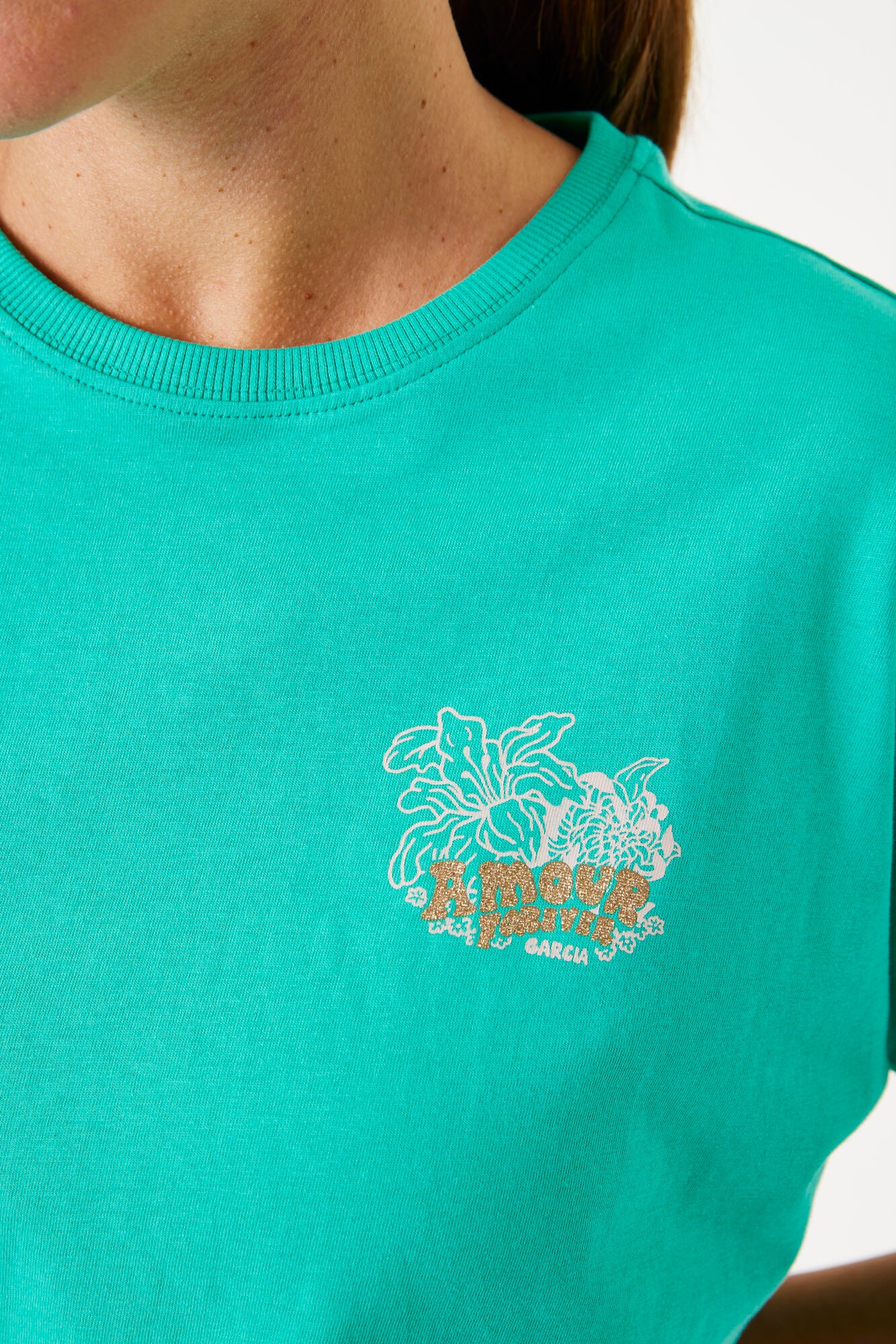 Teal t-shirt with floral design and text on a plain background
