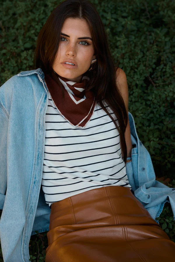 Woman wearing a striped shirt, brown leather pants, and a denim jacket with a brown scarf.