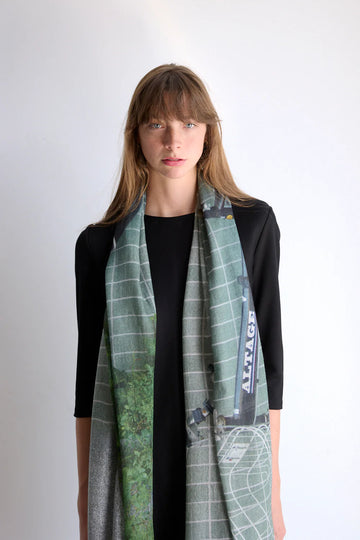 Wool scarf in grey and green tones with word Altage on it. Model. 