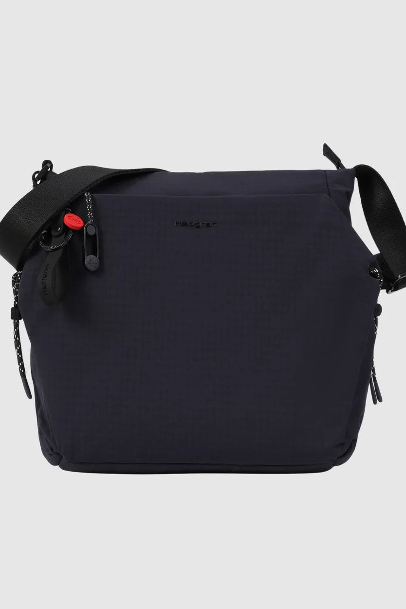 A dark navy blue crossbody bag with a textured, grid-like pattern, featuring a black adjustable shoulder strap, black zipper pulls, and a small red accent on the zipper pull. The brand name 'HABIT' is subtly printed in black on the front.