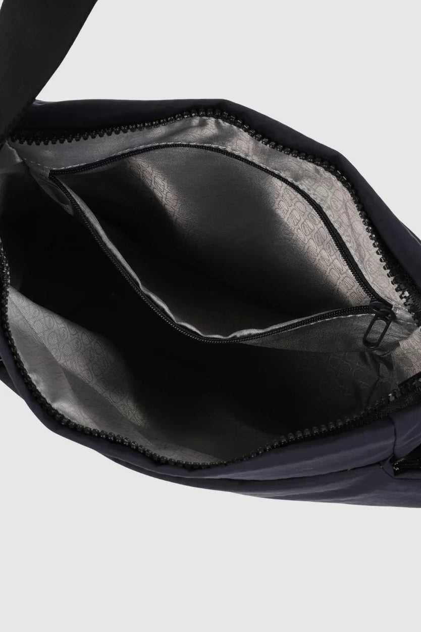 Close-up of an open dark navy crossbody bag showing the black interior lining and zipper compartments against a light gray background.