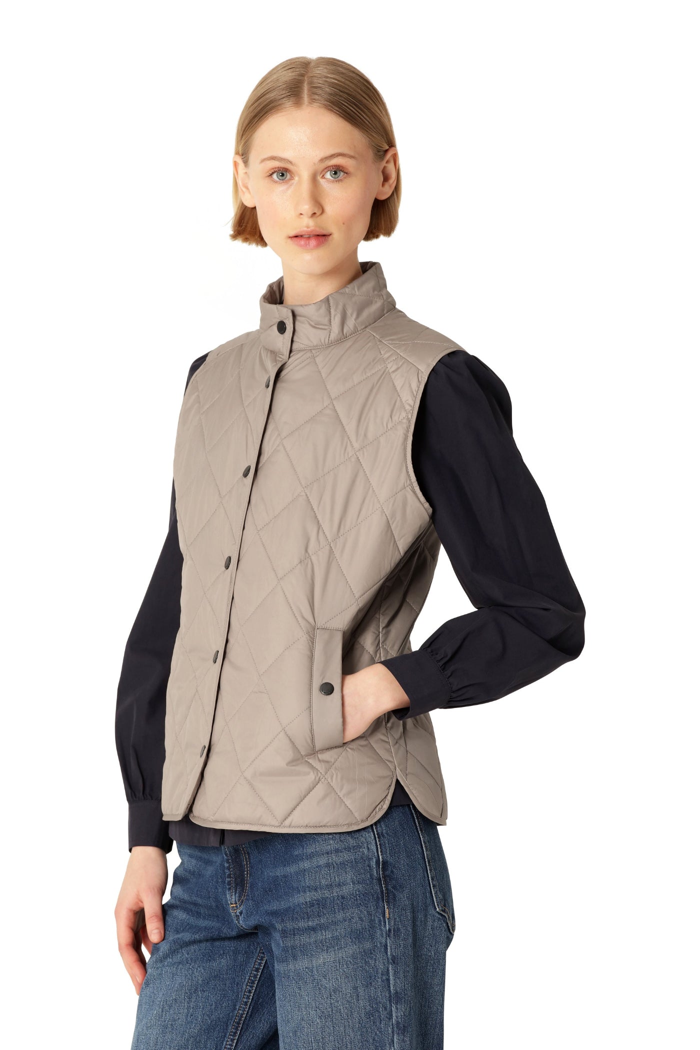 Woman wearing a beige quilted vest over a black shirt on a white background