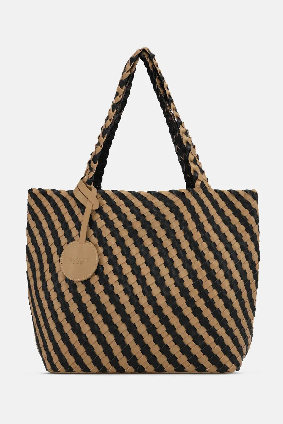 A woven tote bag with a diagonal black and tan pattern, featuring braided shoulder straps and a round tan leather hangtag on a light gray background.