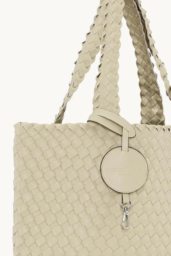 Close up of the straps and tag of  light ivory woven  tote bag with braided shoulder straps and a round hanging tag, shown against a plain white background.