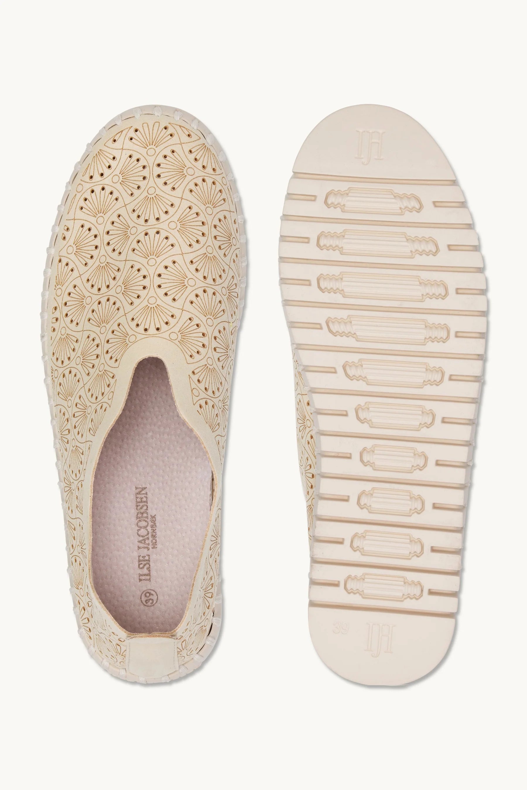 A pair of beige slip-on sneakers with intricate floral cutout embroidery on the upper and a textured, wavy sole, shown against a plain off-white background.