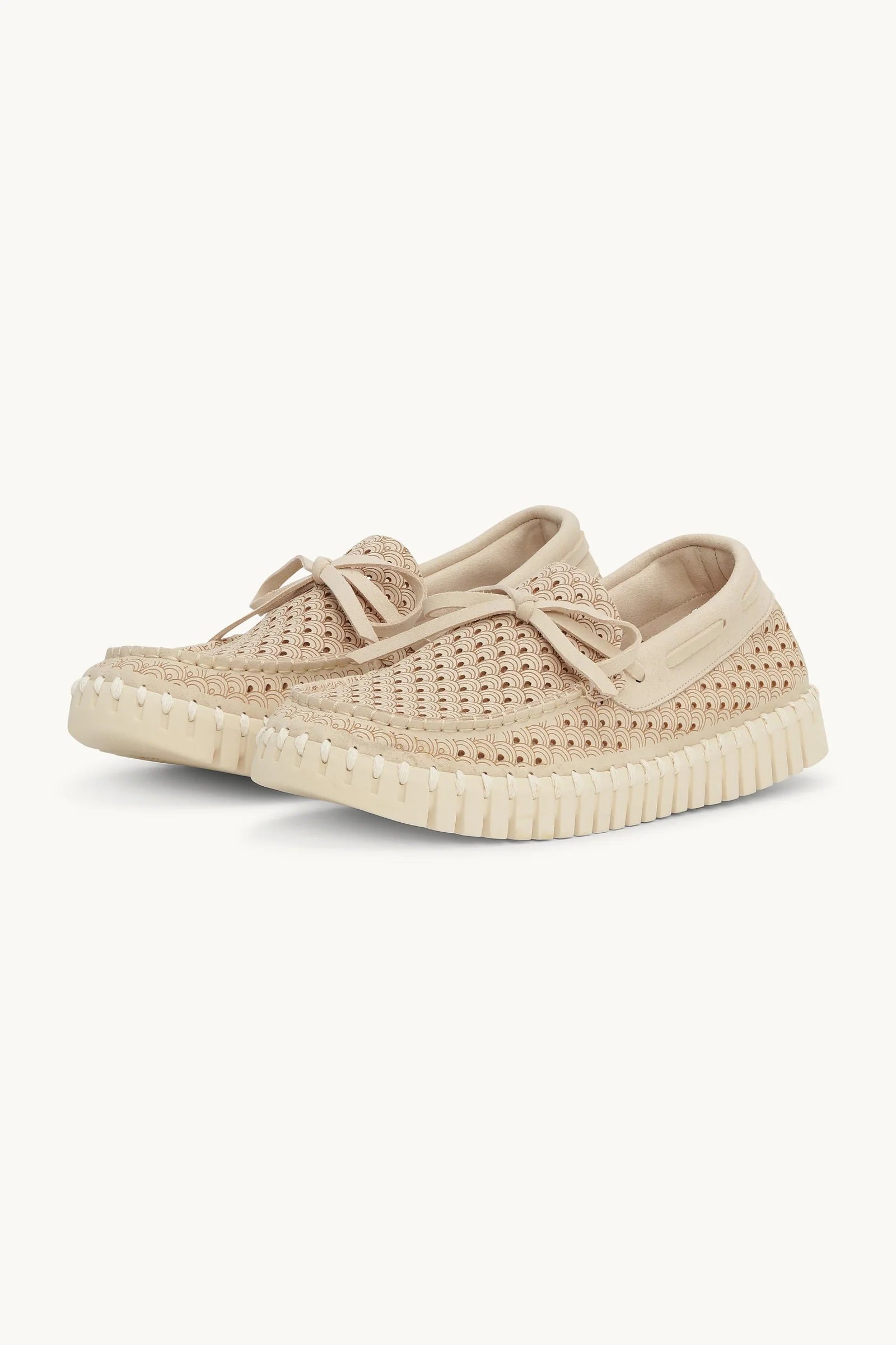 Pari of beige woven slip-on loafers with a matching fabric tie detail on the vamp and a thick, textured off-white sole, shown against a plain off-white background.