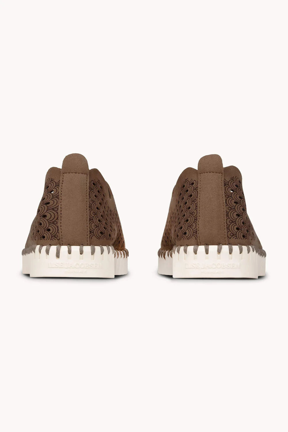 Pair of brown slip on shoes with lazer cut patter and white rubber soles on a plain background. 