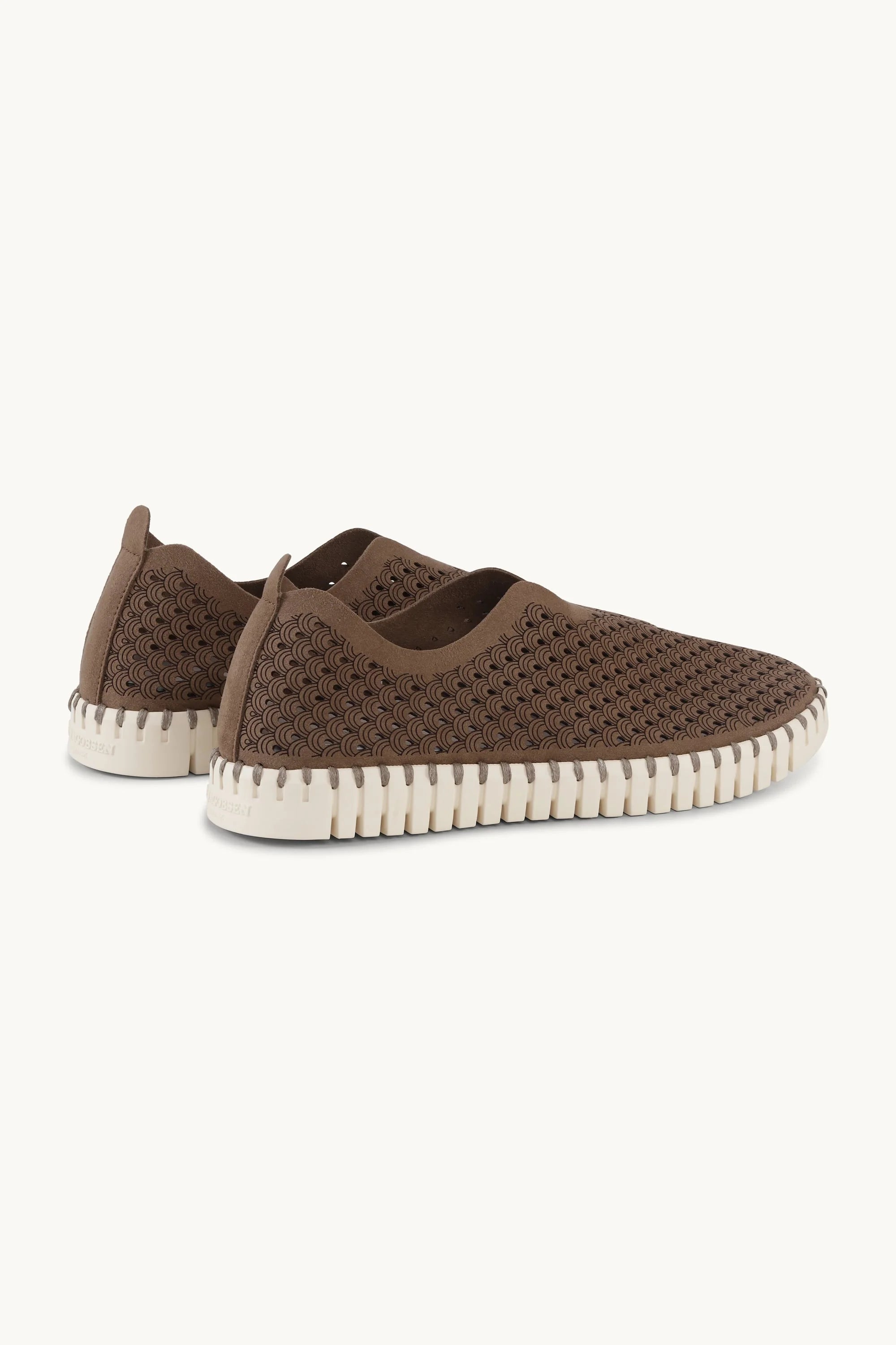 Brown slip-on sneakers with white soles on a light beige background