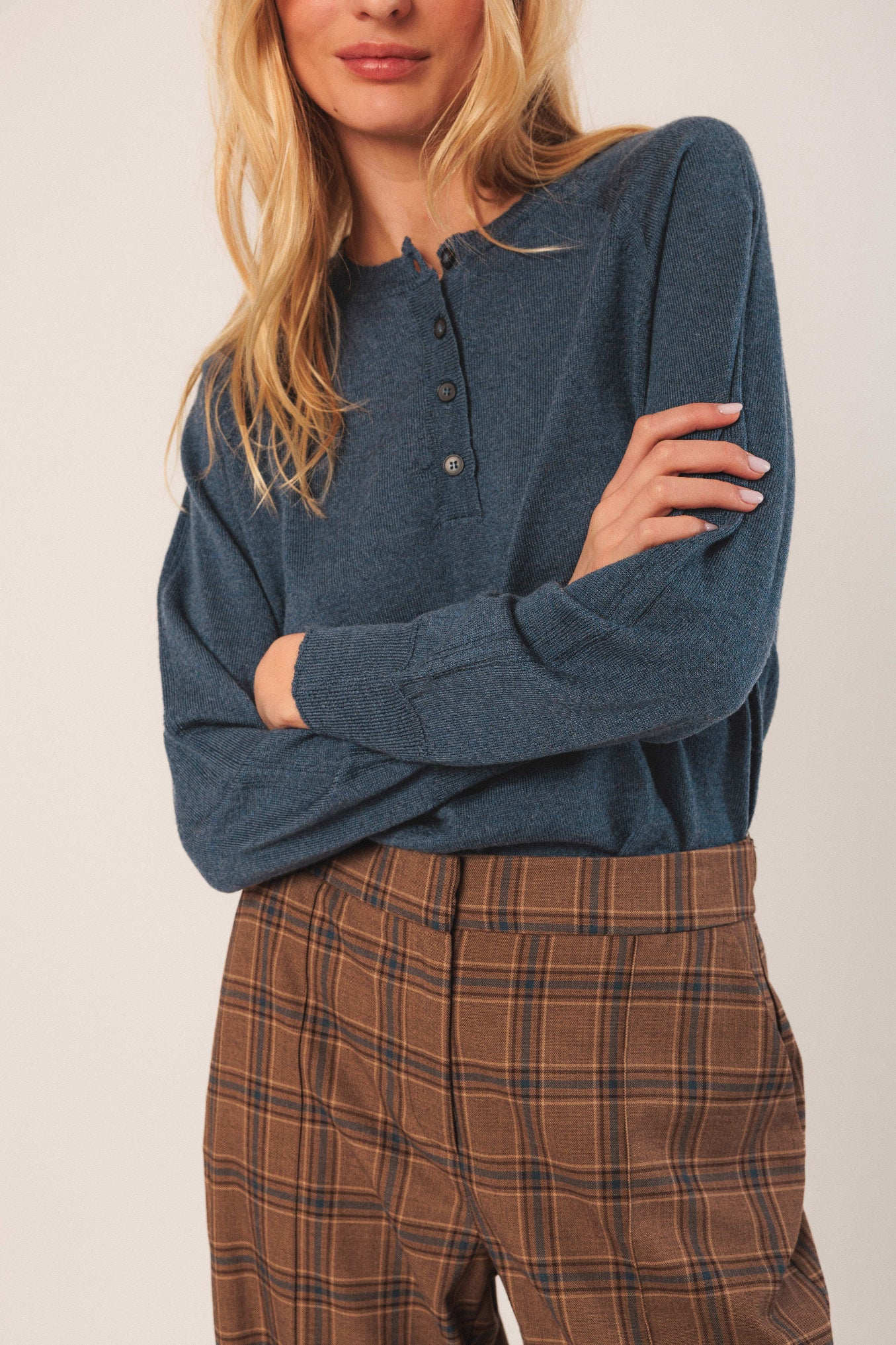 Woman wearing a blue long-sleeve shirt and plaid pants against a plain background