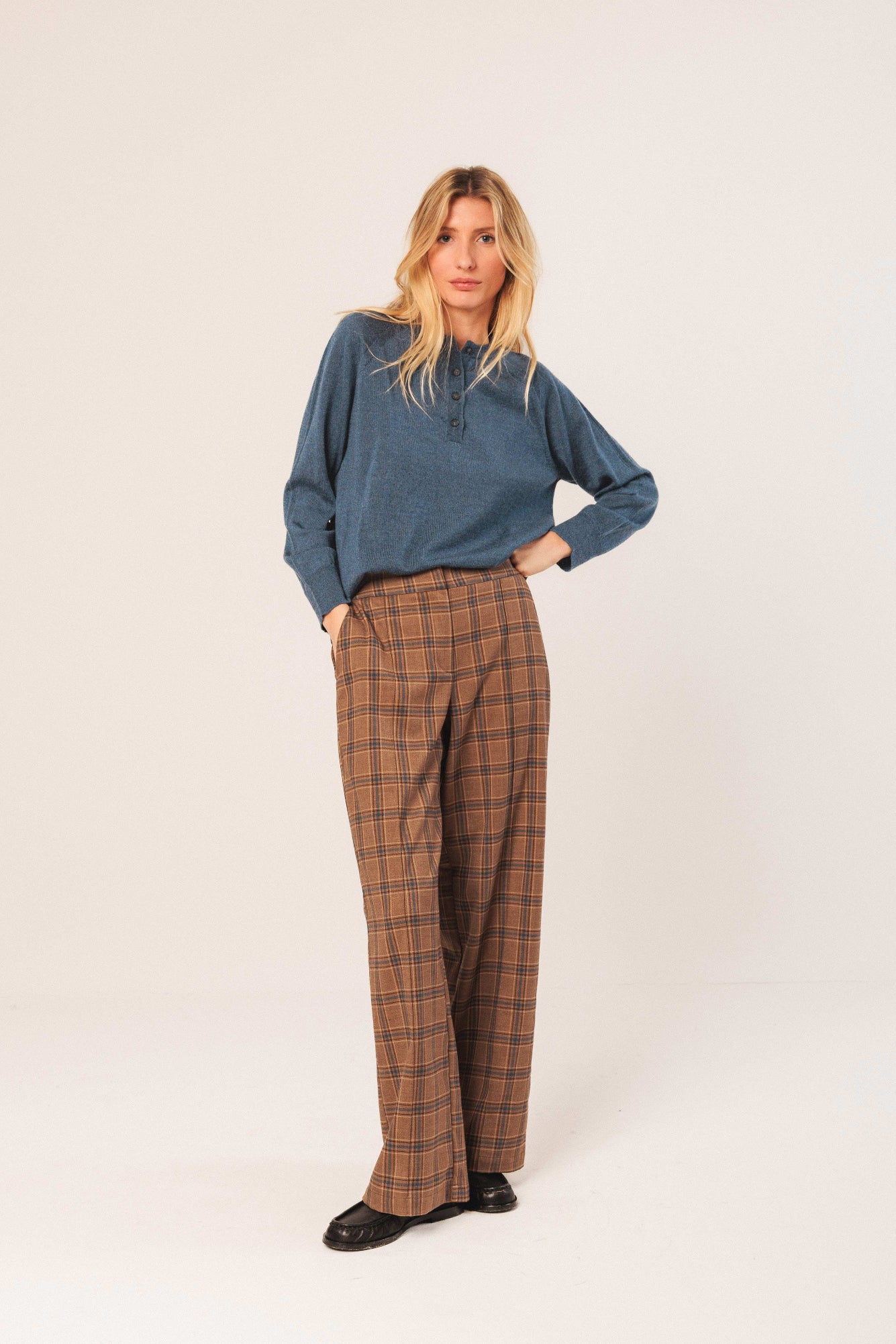 Woman wearing a blue sweater and plaid pants on a white background