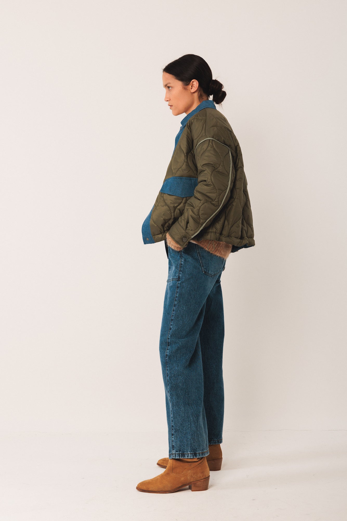 Person wearing a green jacket with blue accents and blue jeans on a white background