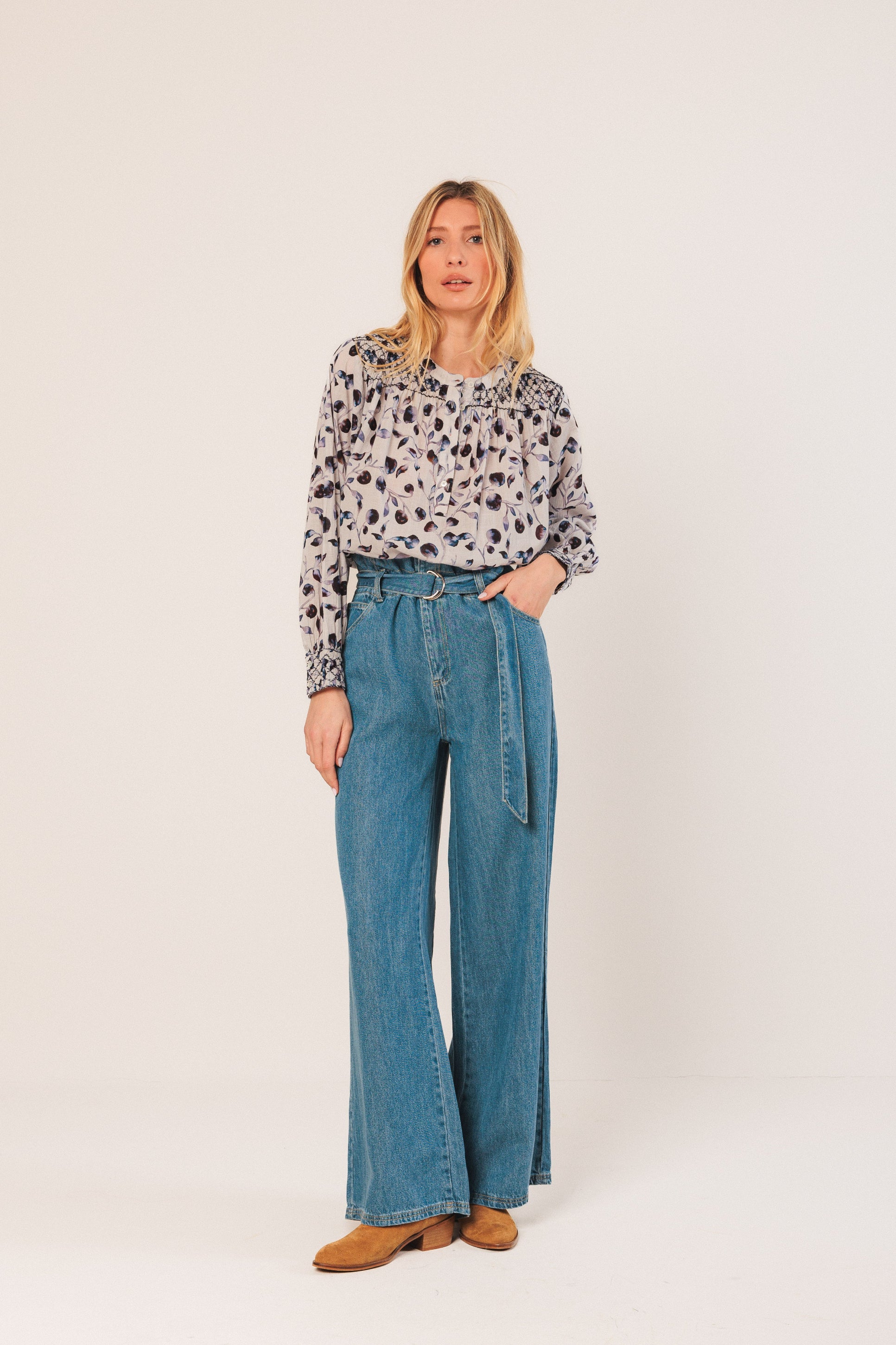 Woman wearing a patterned blouse and blue jeans on a white background
