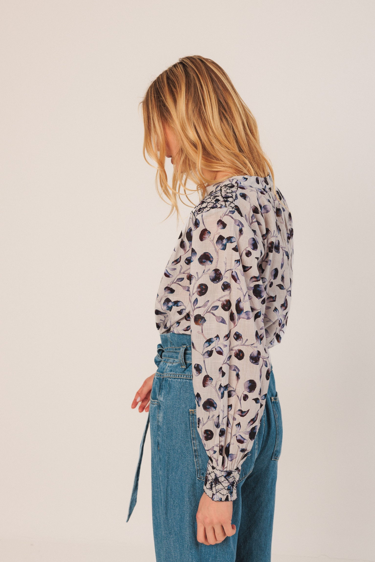 Person wearing a patterned long-sleeve top and blue jeans against a plain background