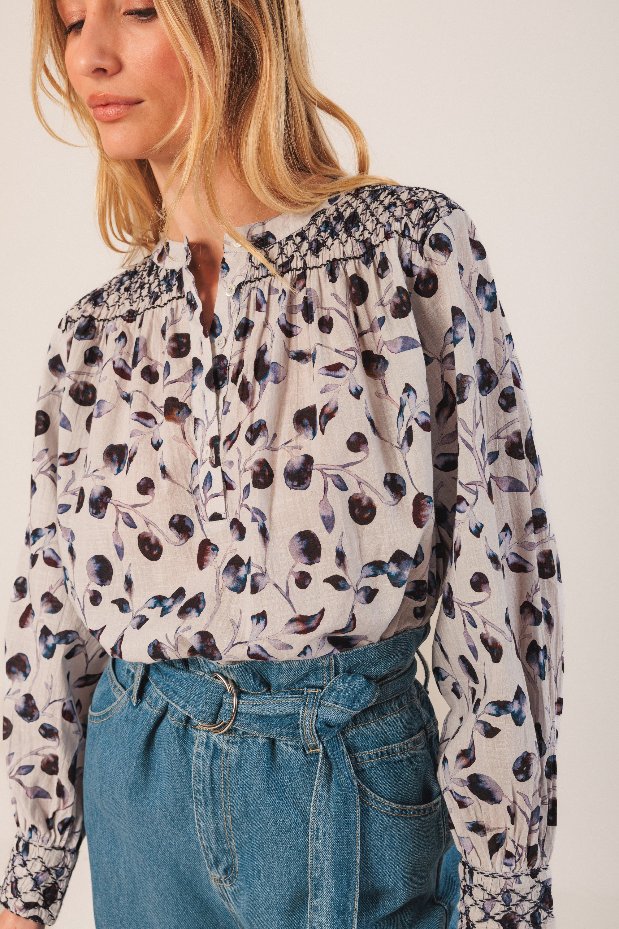 Woman wearing a floral blouse and blue jeans against a white background