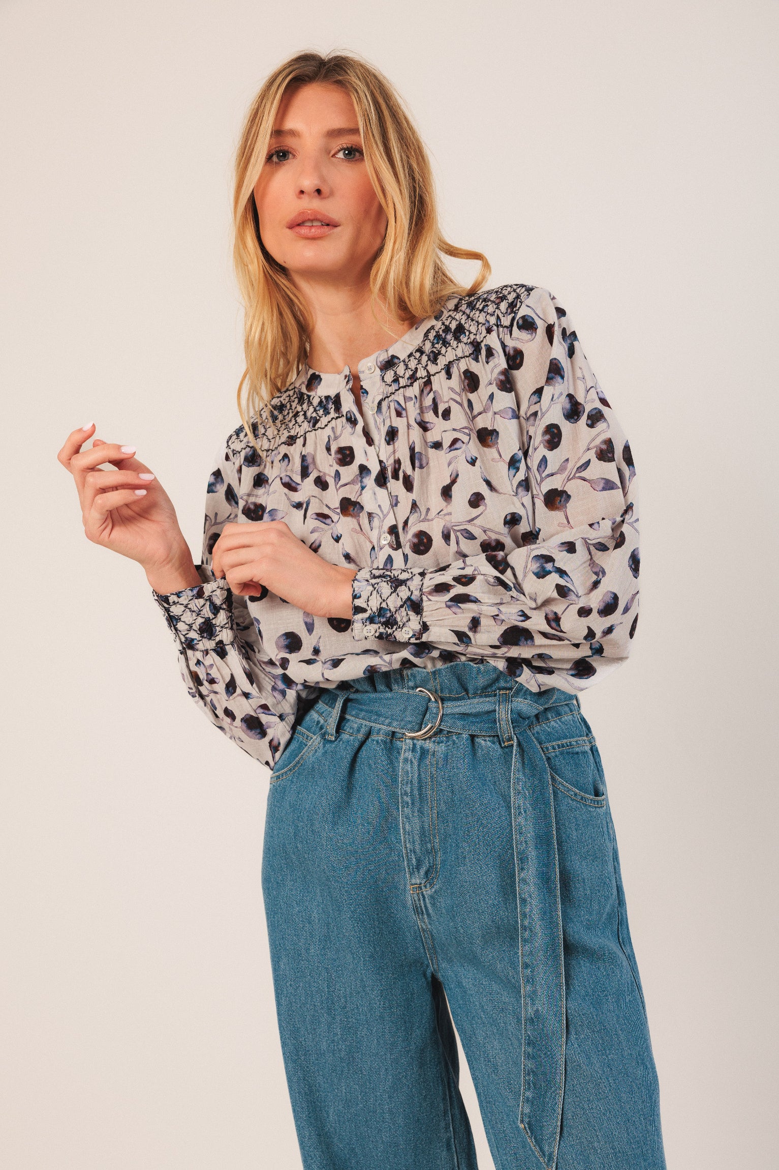 Woman wearing a patterned blouse and blue jeans against a plain background