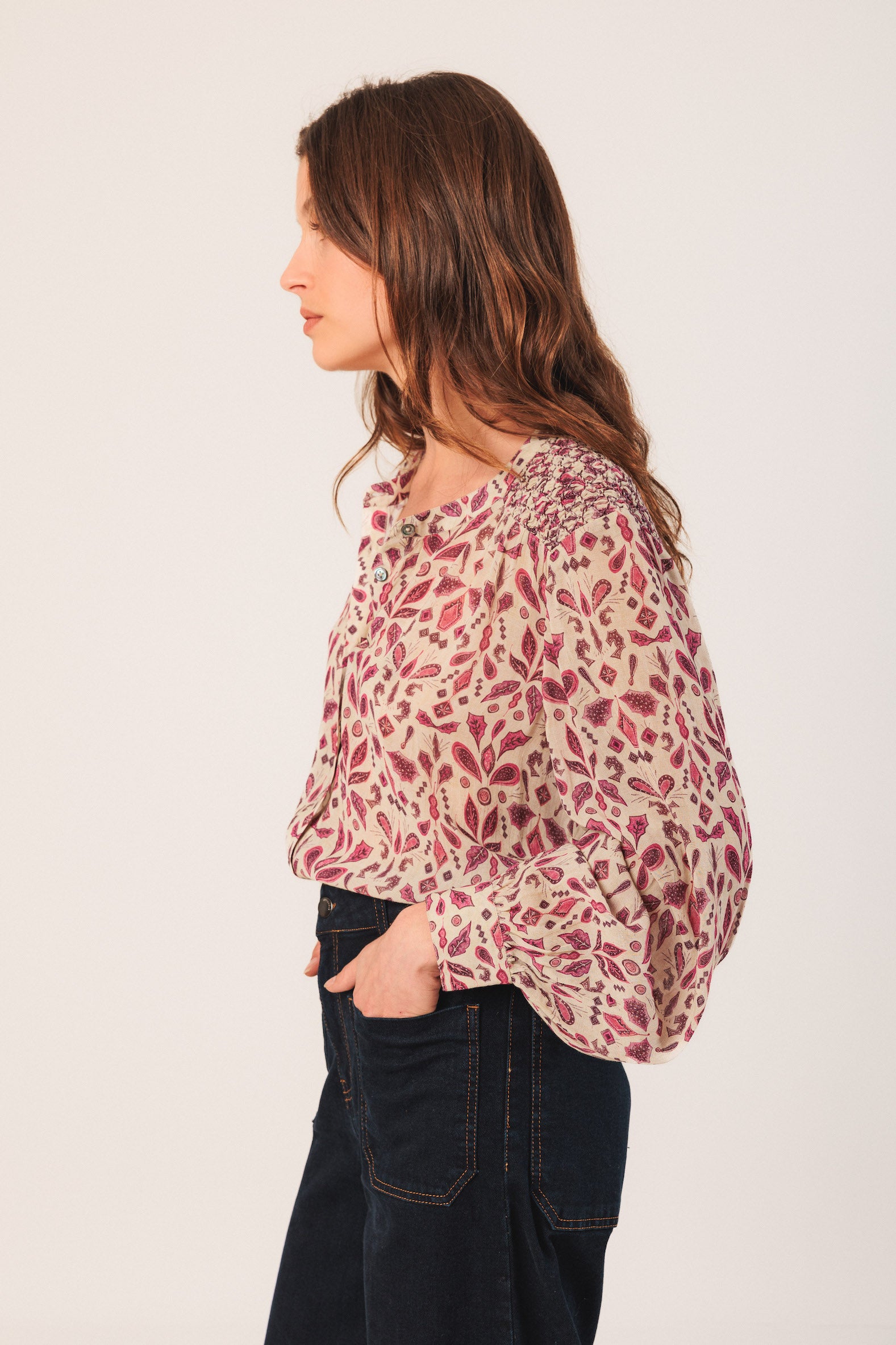 Woman wearing a patterned blouse and dark jeans on a plain background