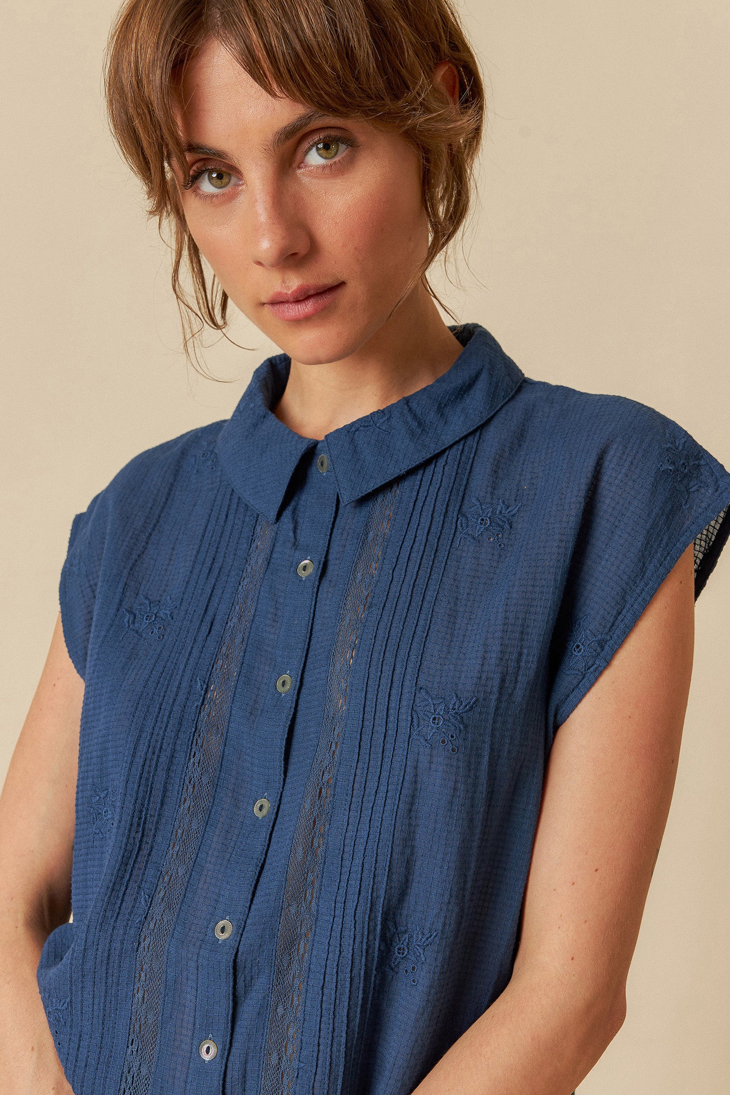 Model wearing a blue sleeveless blouse denim jeans on a beige background. 