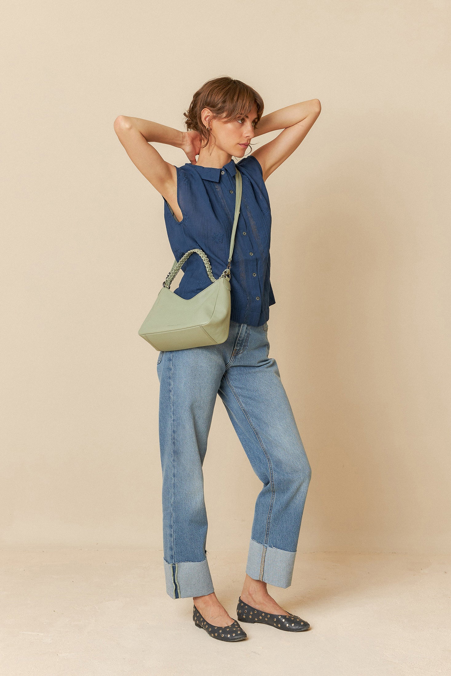Model wearing a blue sleeveless blouse denim jeans on a beige background. 