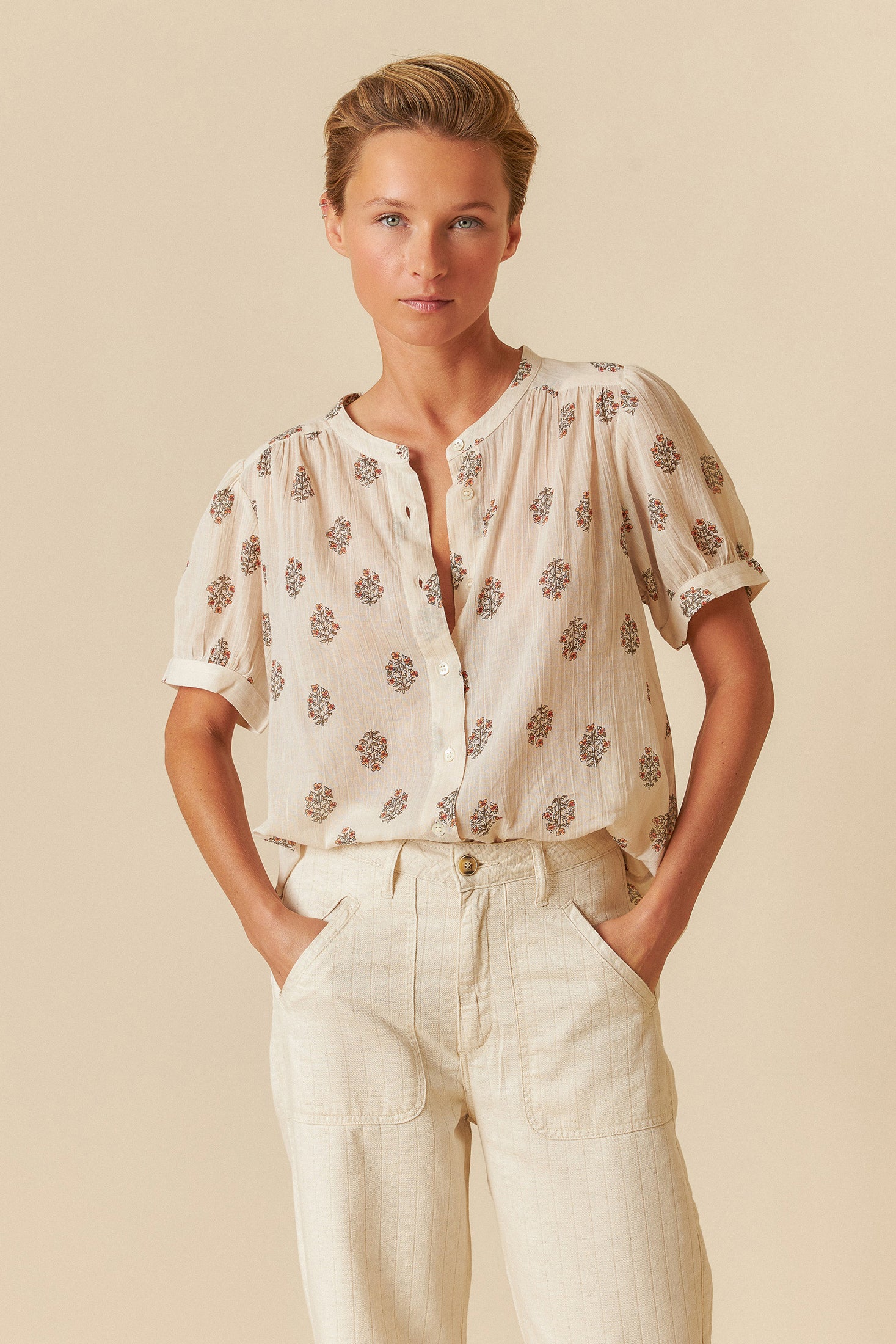 Woman wearing a white blouse with floral patterns and white pants on a beige background