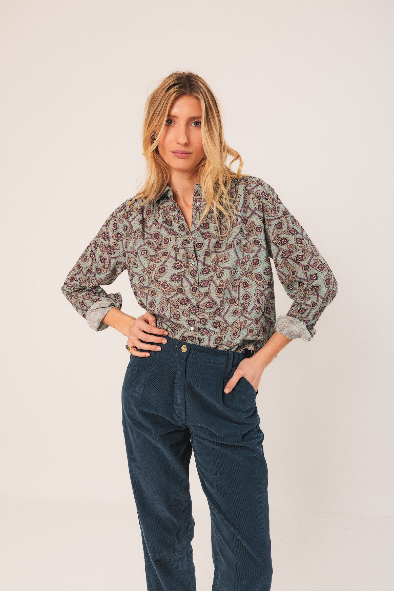 Woman wearing a patterned shirt and blue pants on a white background