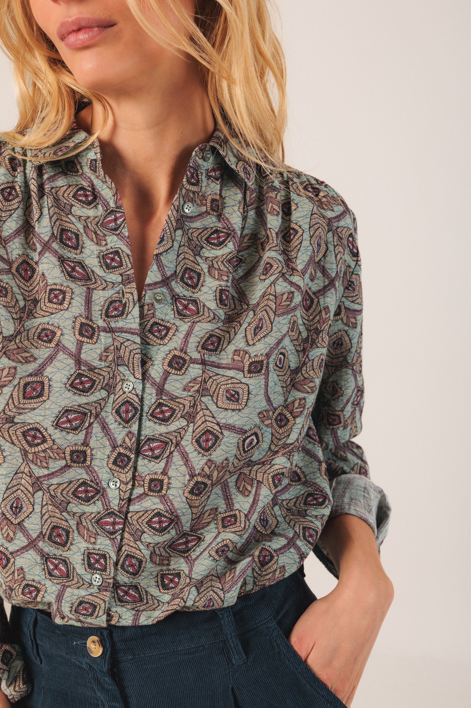 Woman wearing a patterned shirt with rolled-up sleeves on a plain background