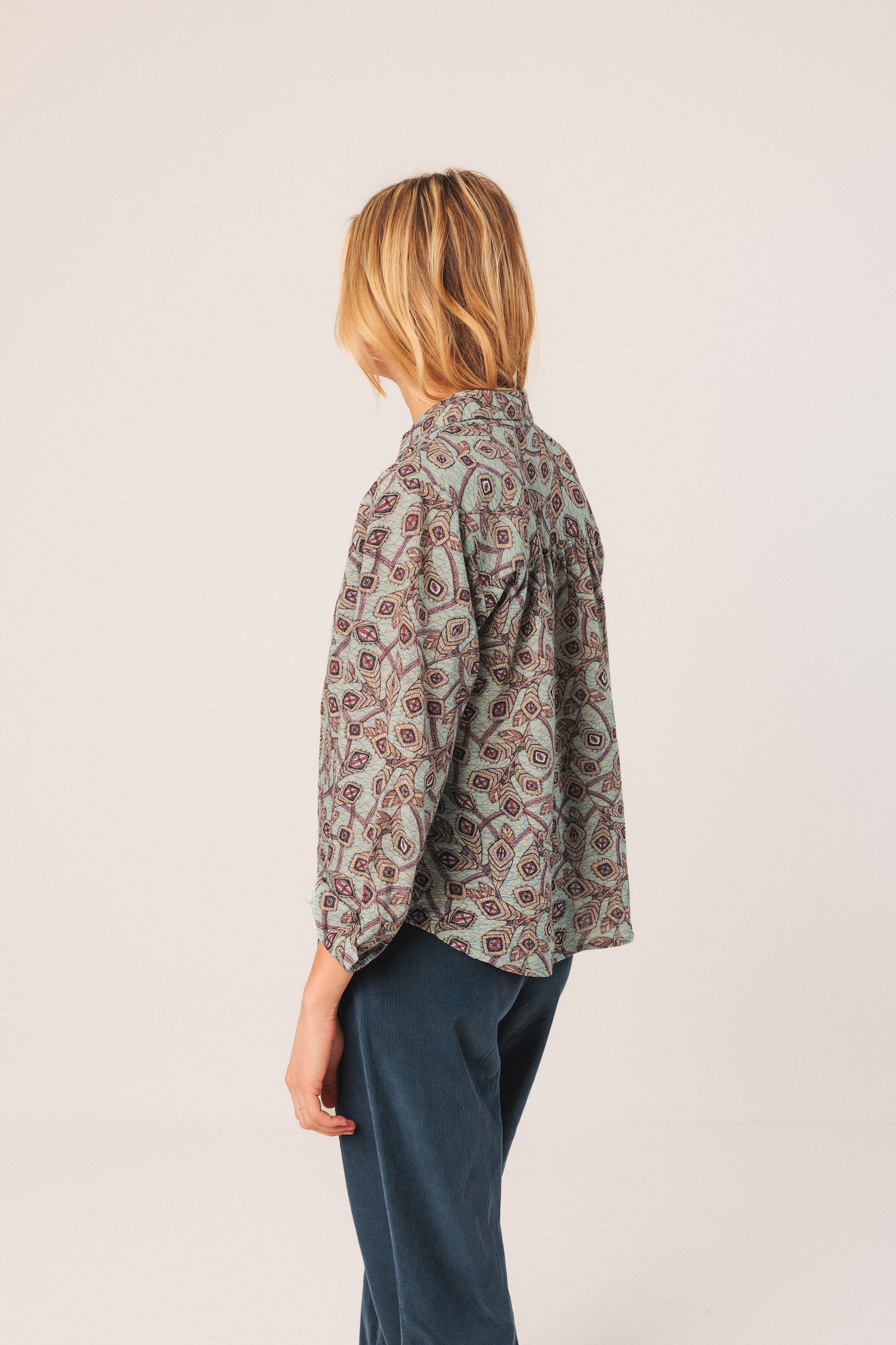 Person wearing a patterned shirt and dark pants on a light background