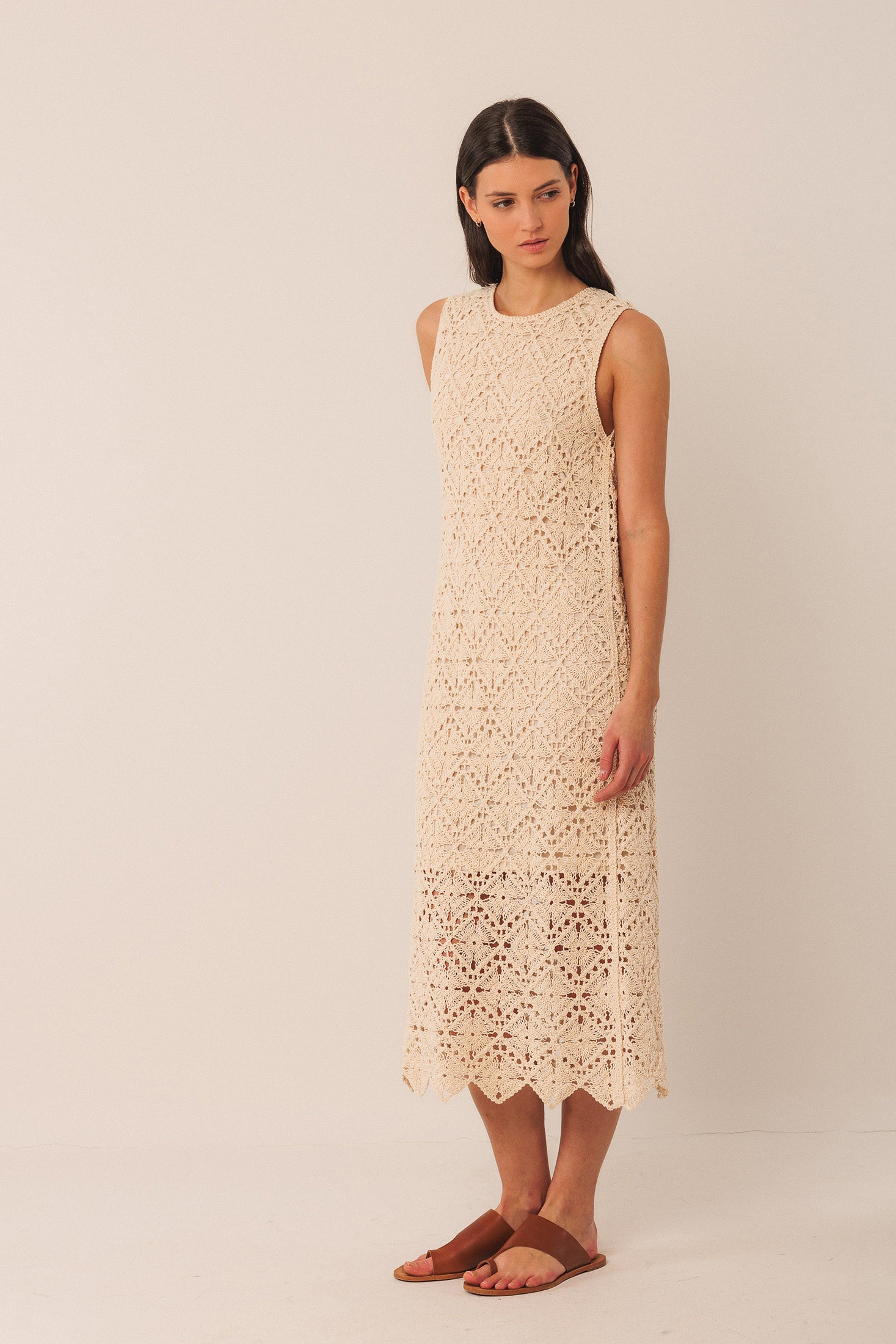 Woman wearing a beige crochet sleeveless midi dress against a plain background
