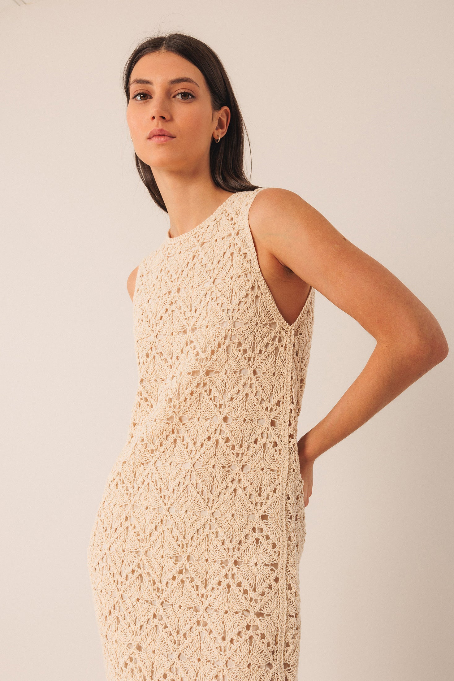 Woman wearing a beige crochet sleeveless midi dress against a plain background