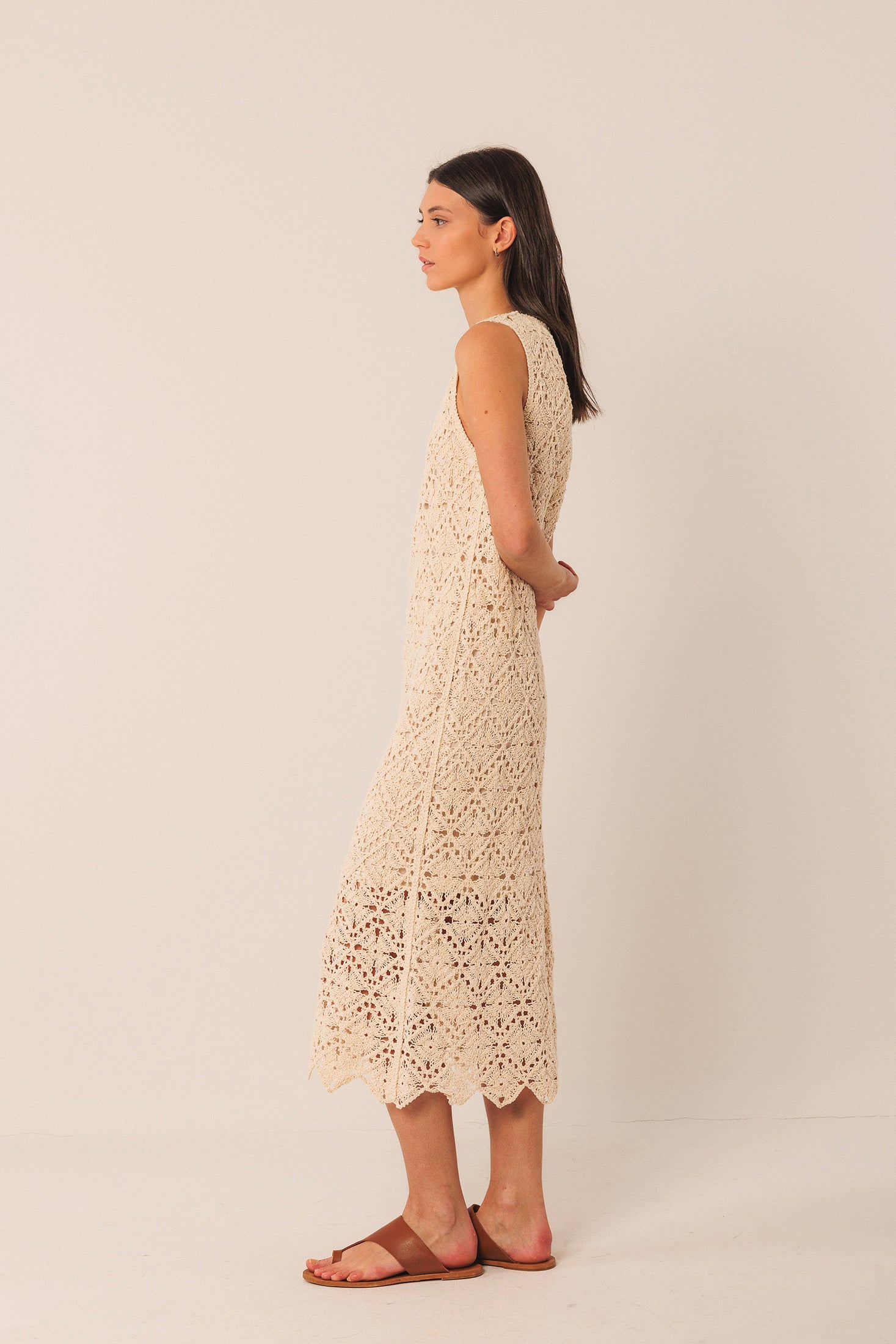 Woman wearing a beige crochet sleeveless midi dress against a plain background