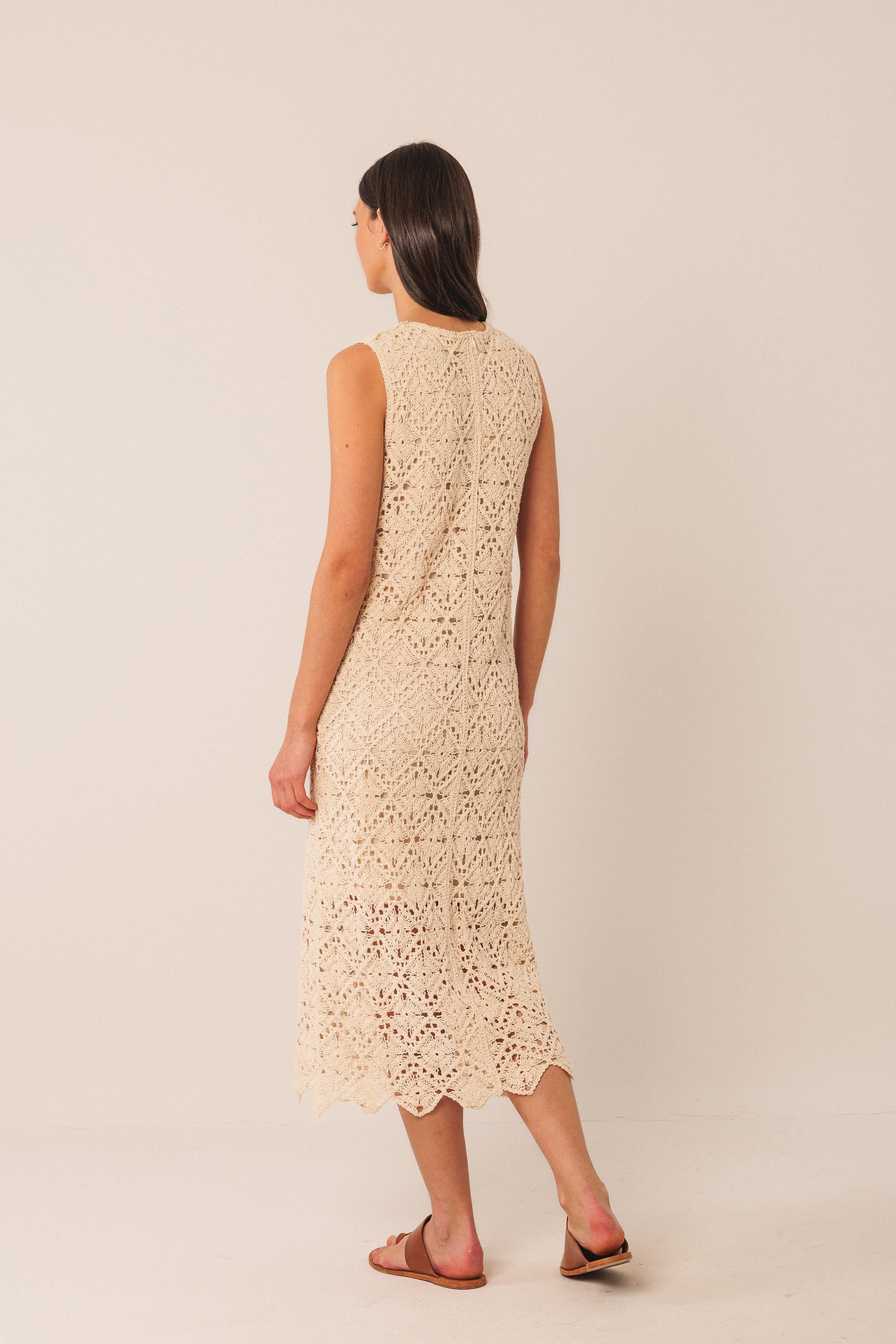 Woman wearing a beige crochet sleeveless midi dress against a plain background