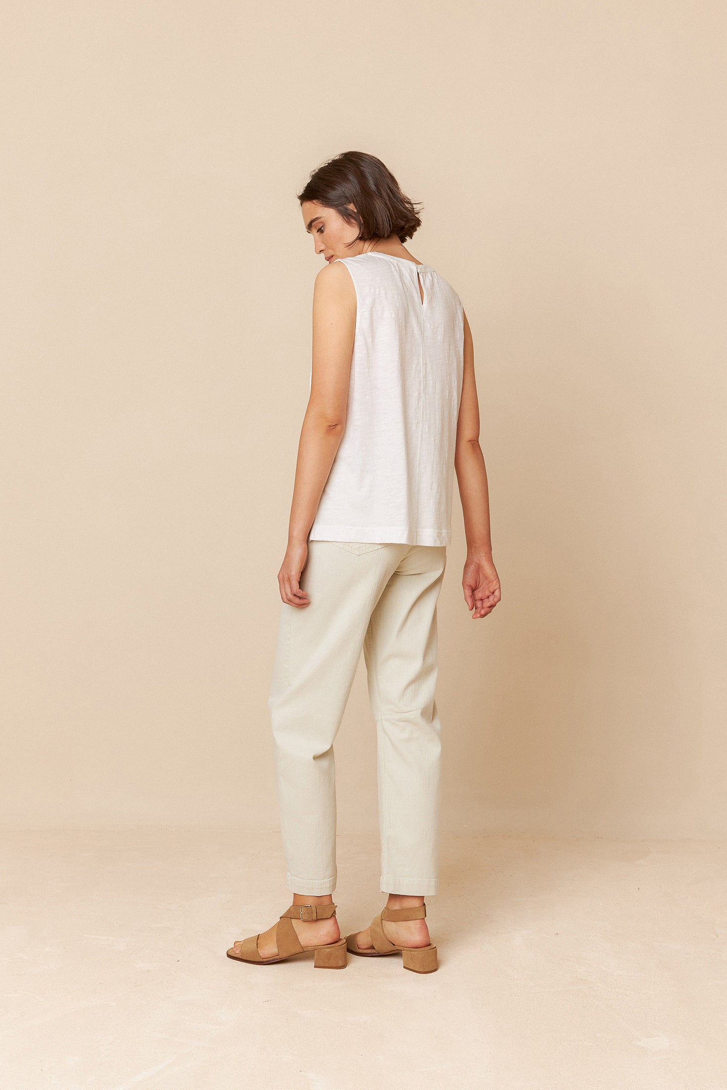 Woman wearing a white sleeveless top and cream pants against a beige background