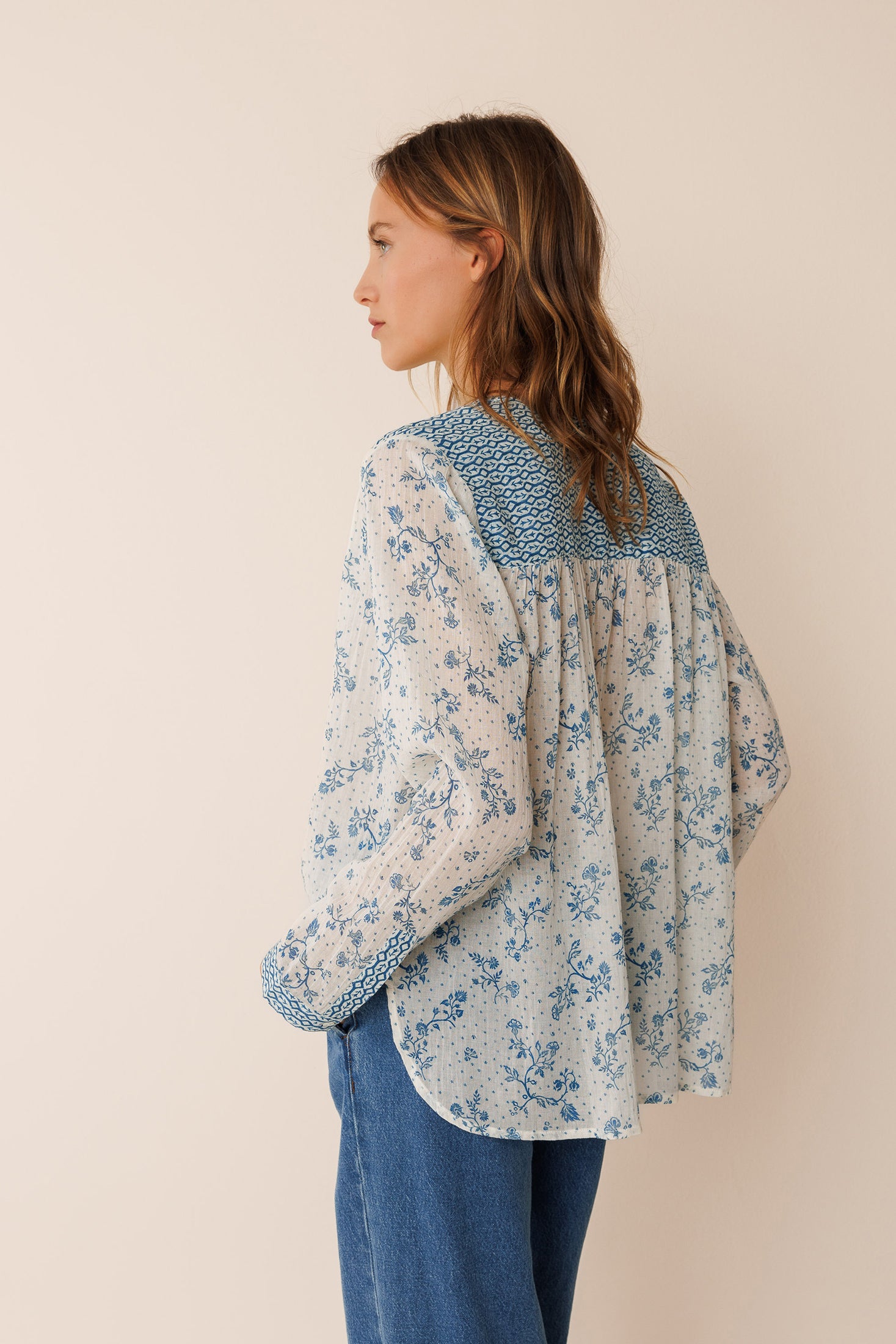 Woman wearing a floral long sleeve cotton blouse and blue jeans against a beige wall
