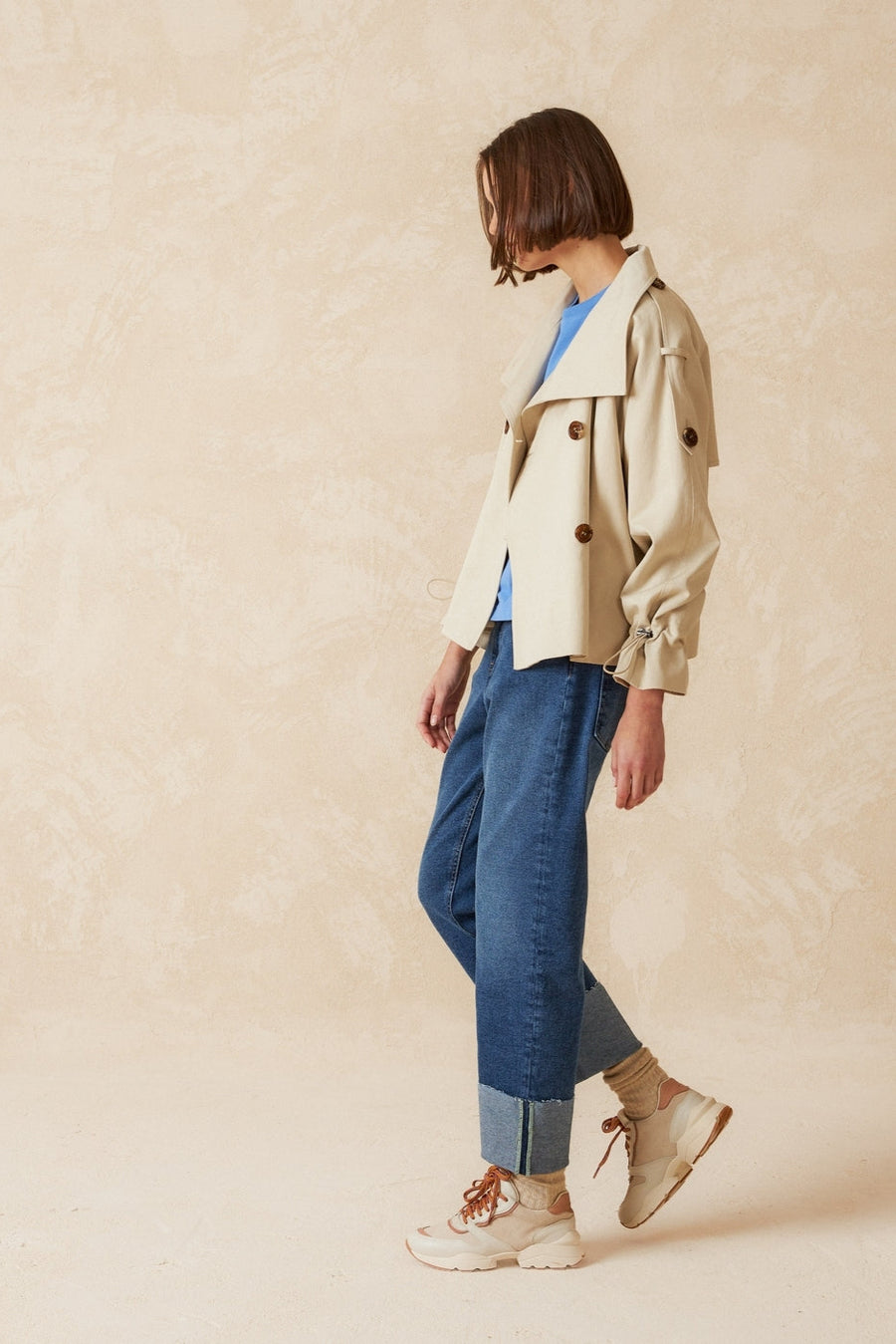 Beige double breasted cropped trench coat with belt.