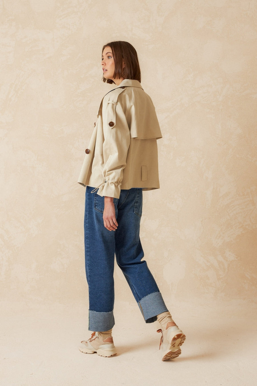 Beige double breasted cropped trench coat with belt.
