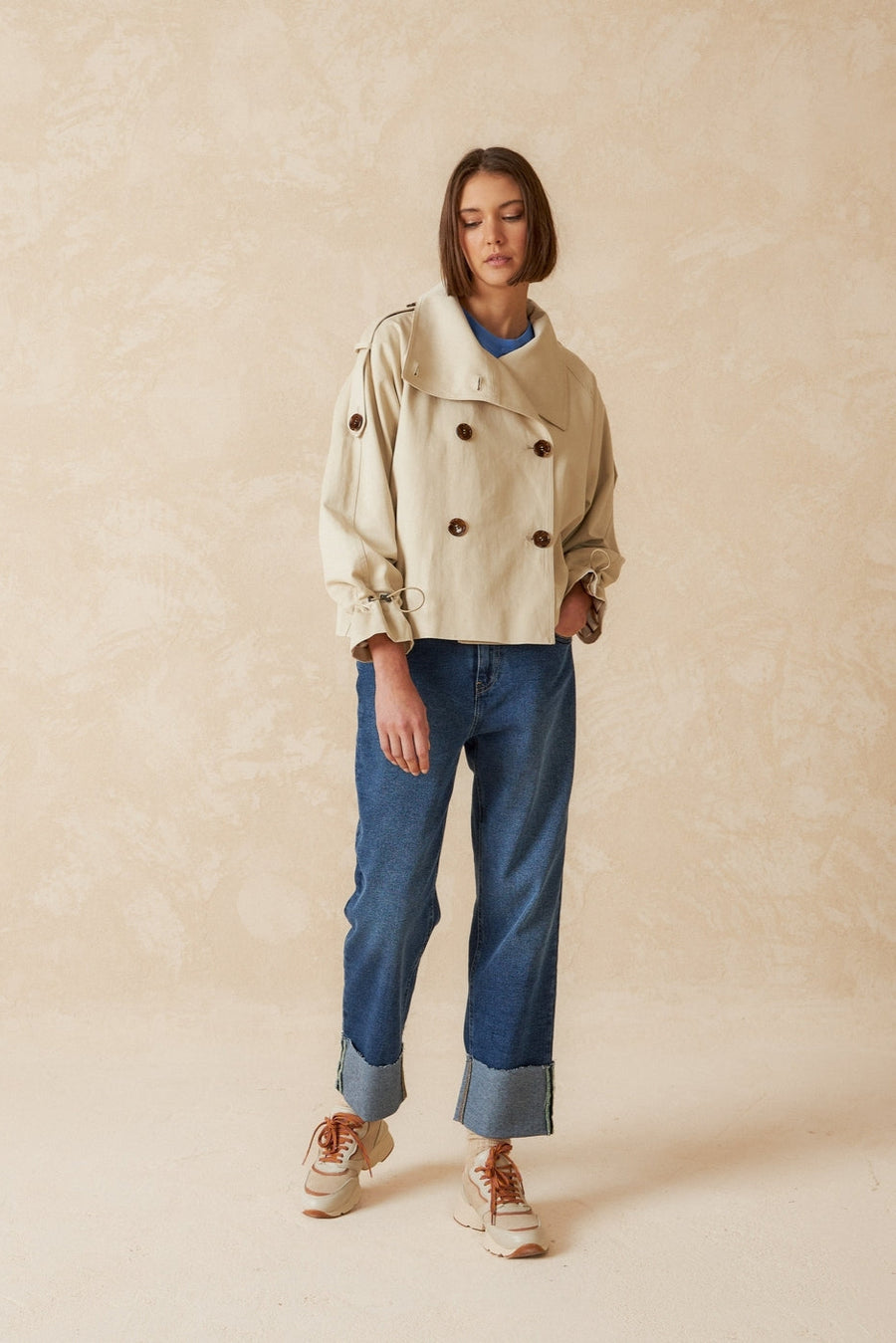 Beige double breasted cropped trench coat with belt.