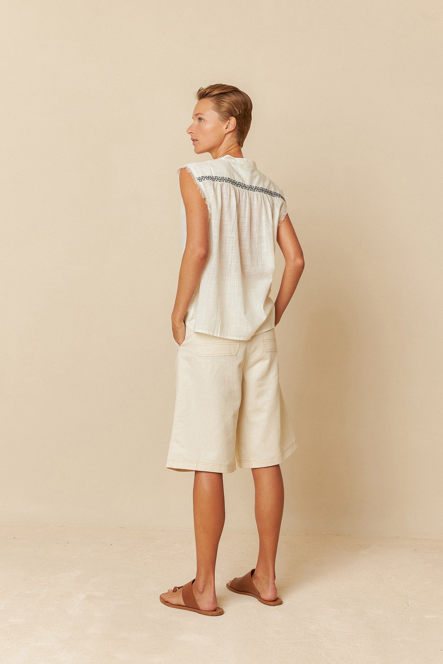 Woman wearing a sleeveless beige top and shorts against a beige background