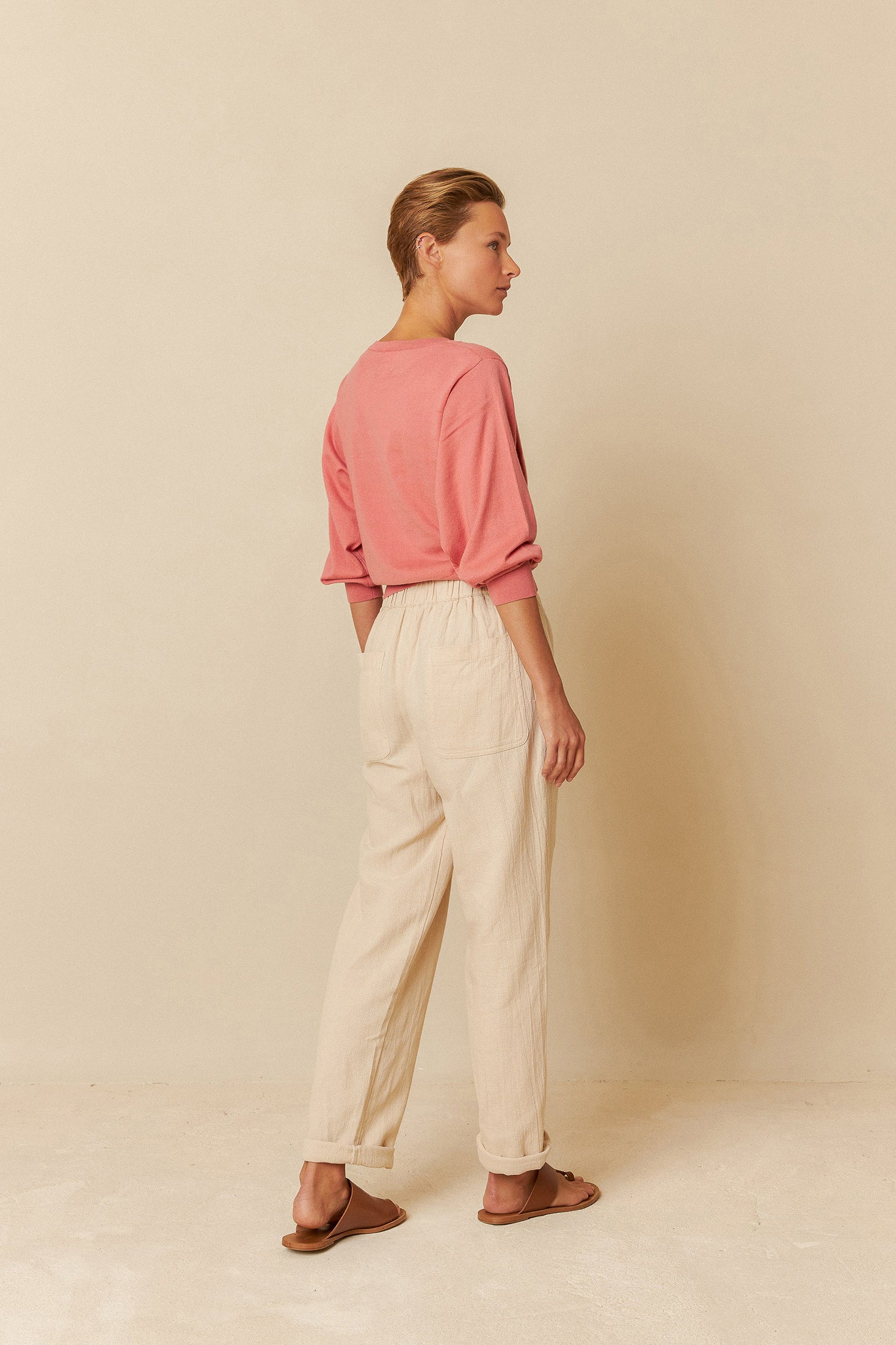 Woman wearing a pink sweater and beige pants against a beige background