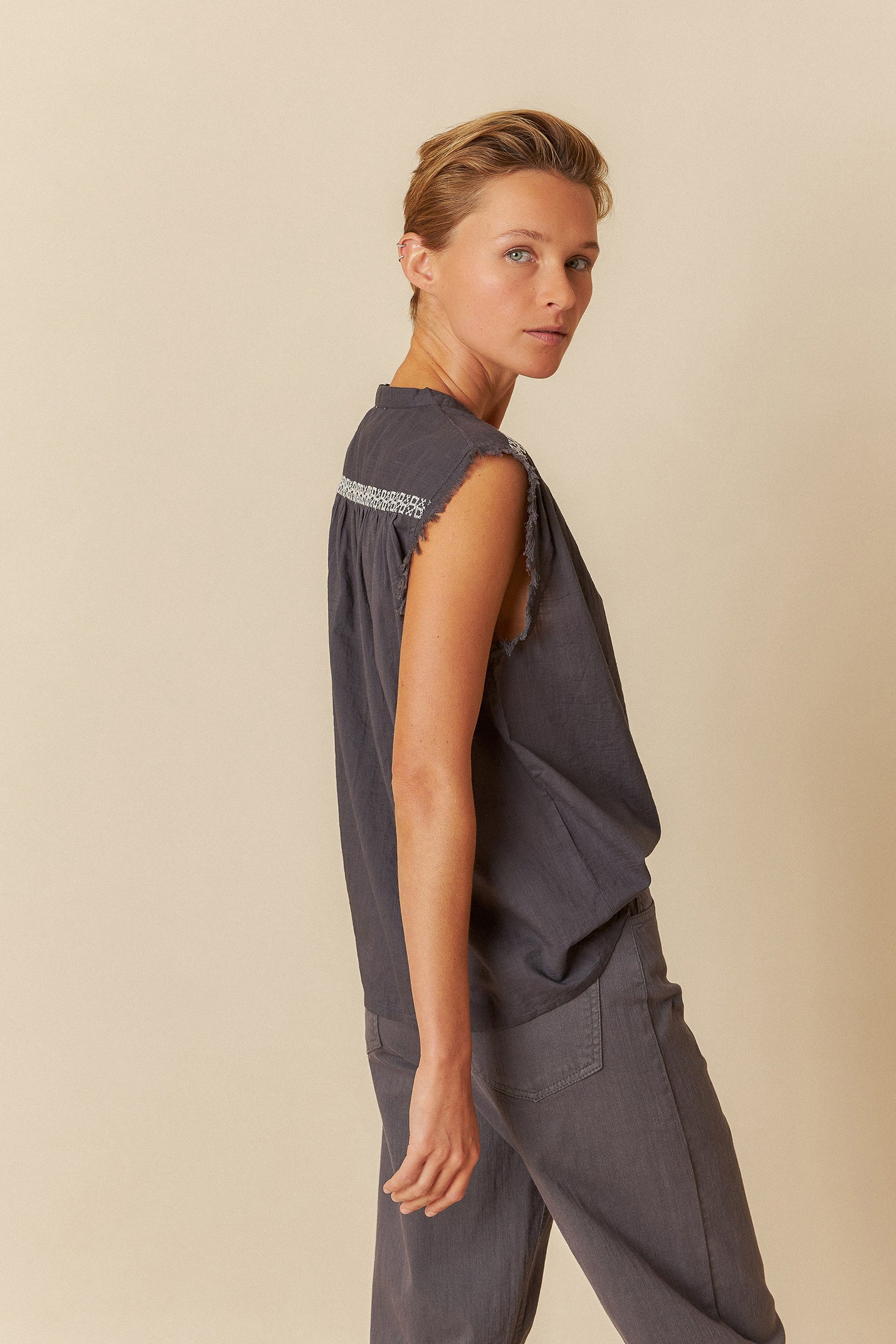 Woman wearing a black sleeveless top with white embroidery and black pants on a light grey background