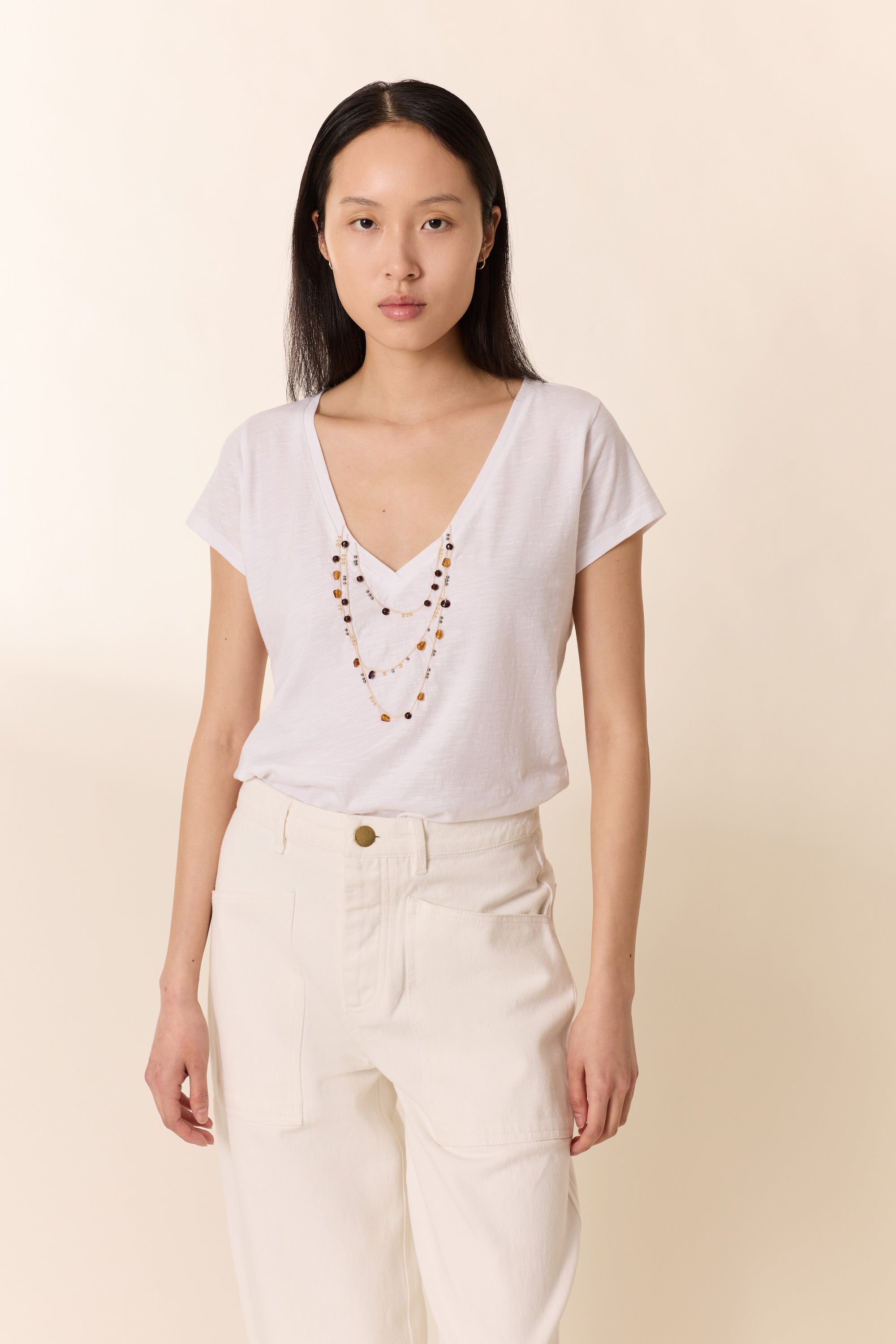 Woman wearing a white top with a V-neckline and beige pants on a beige background