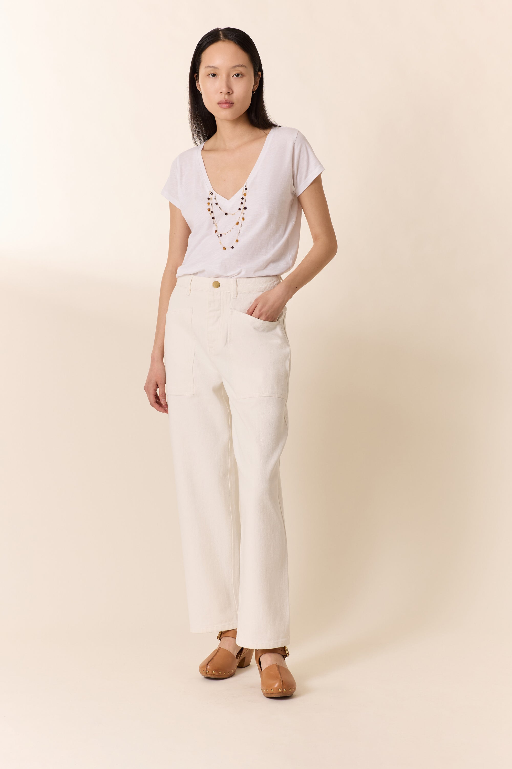 Woman wearing a white top and cream pants against a beige background