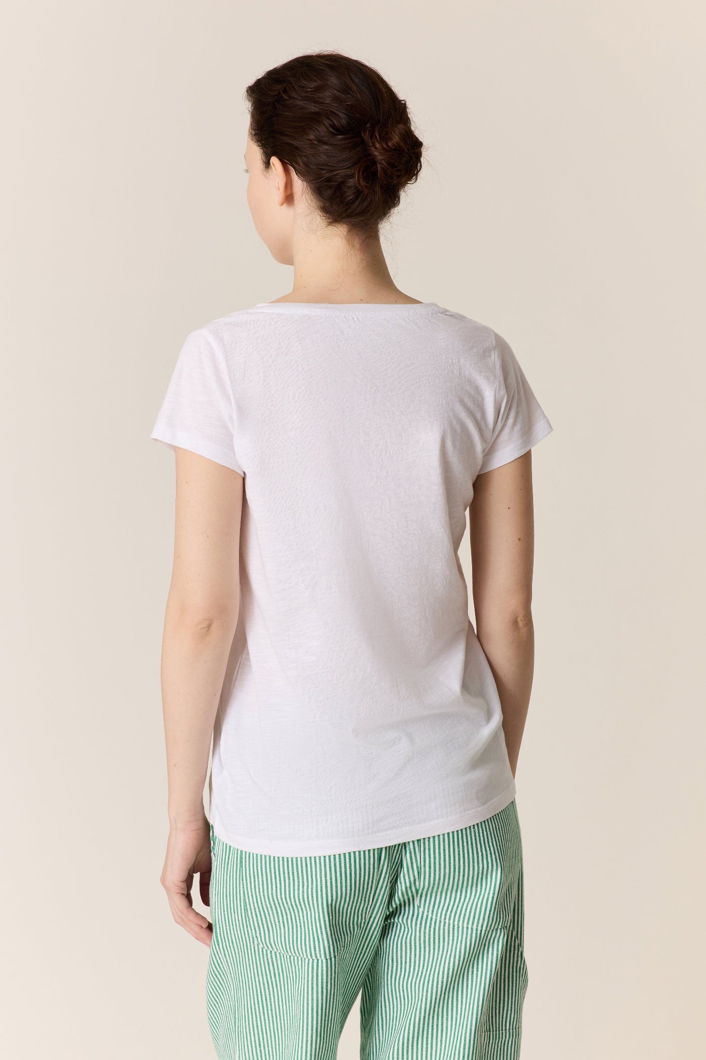Person shown from the back wearing a plain white t-shirt and green pants on a beige background