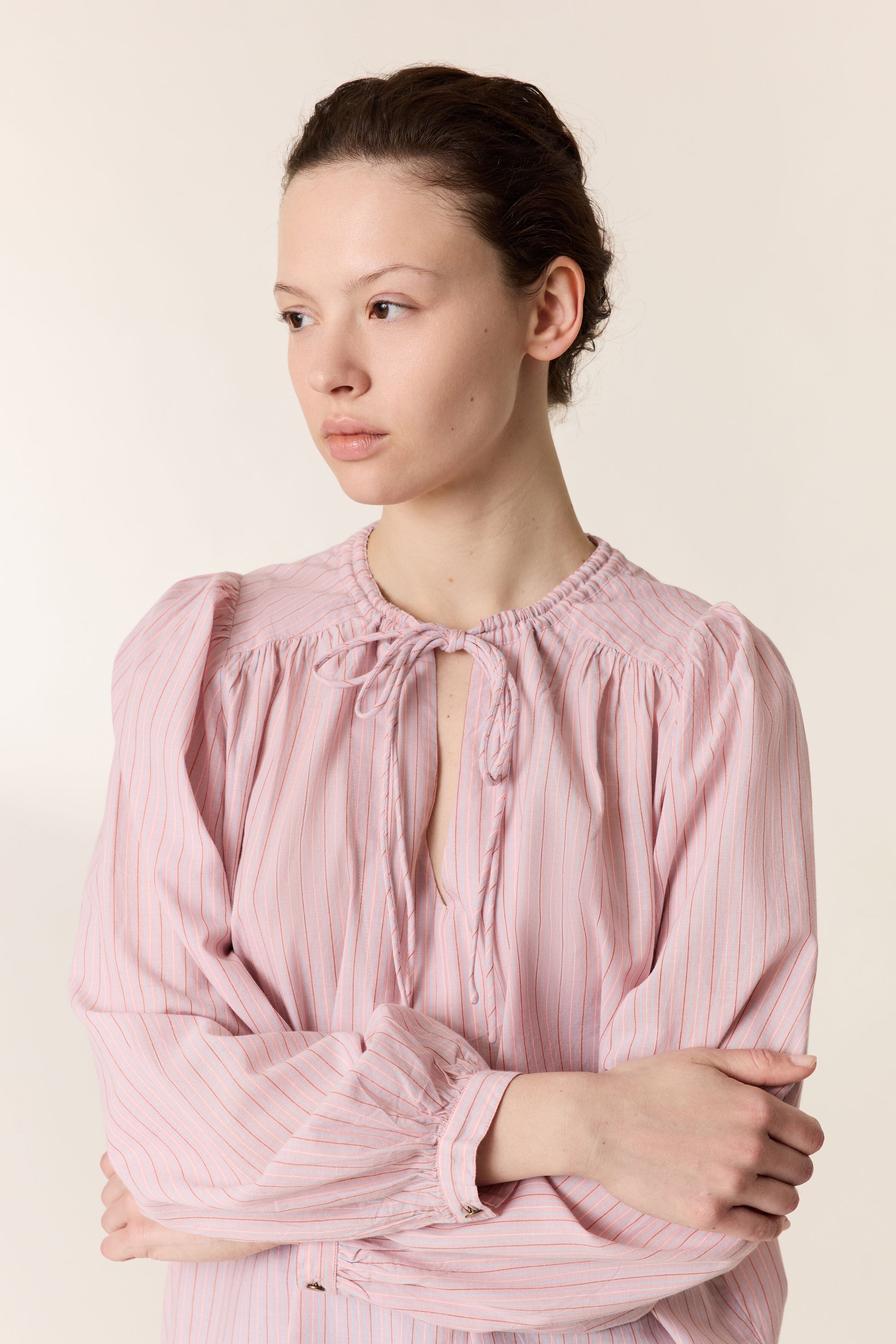 Close up of a woman wearing a pink stripe shirt on a plain background. 