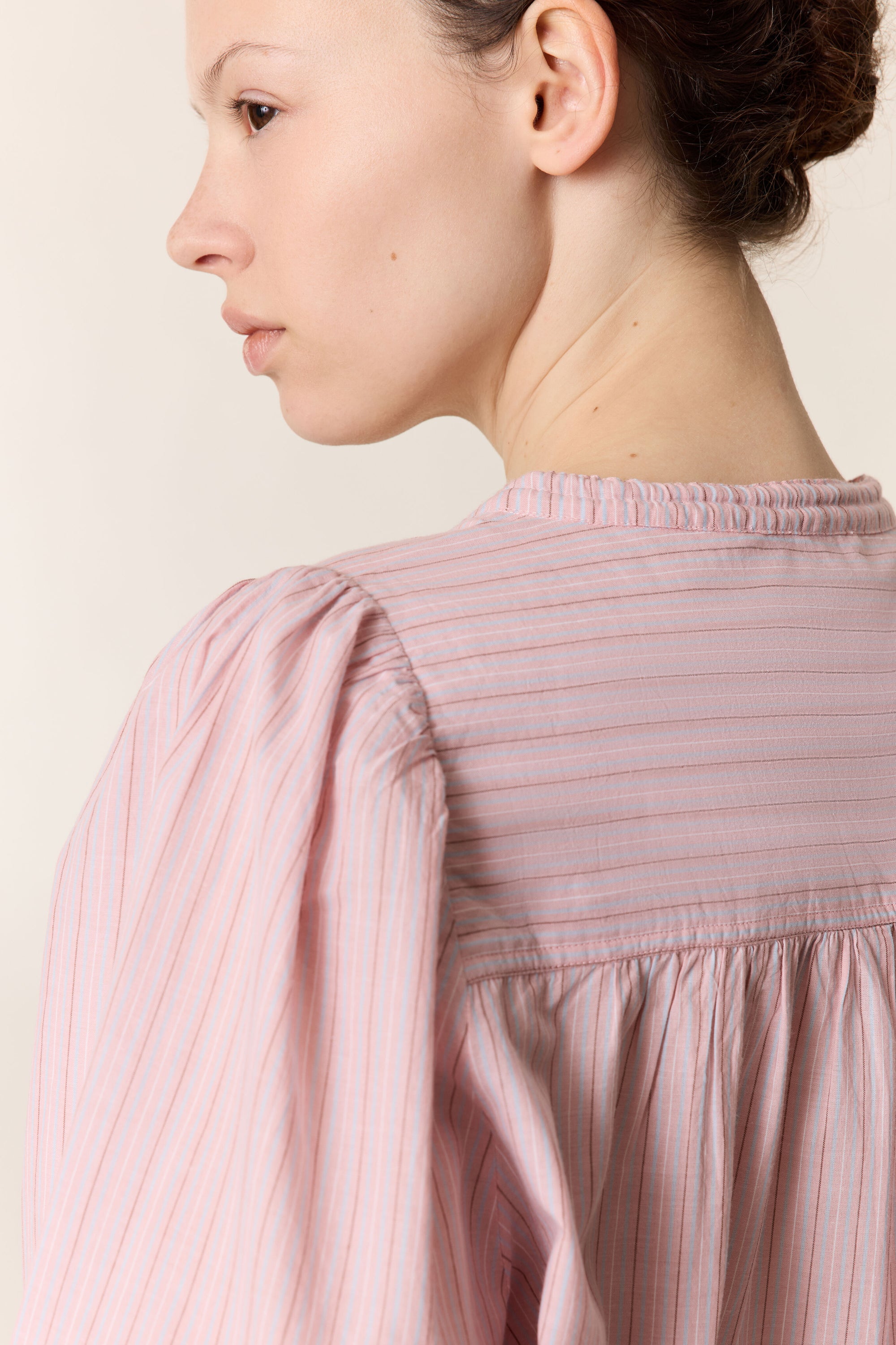 Close up of a woman wearing a pink stripe shirt on a plain background. 