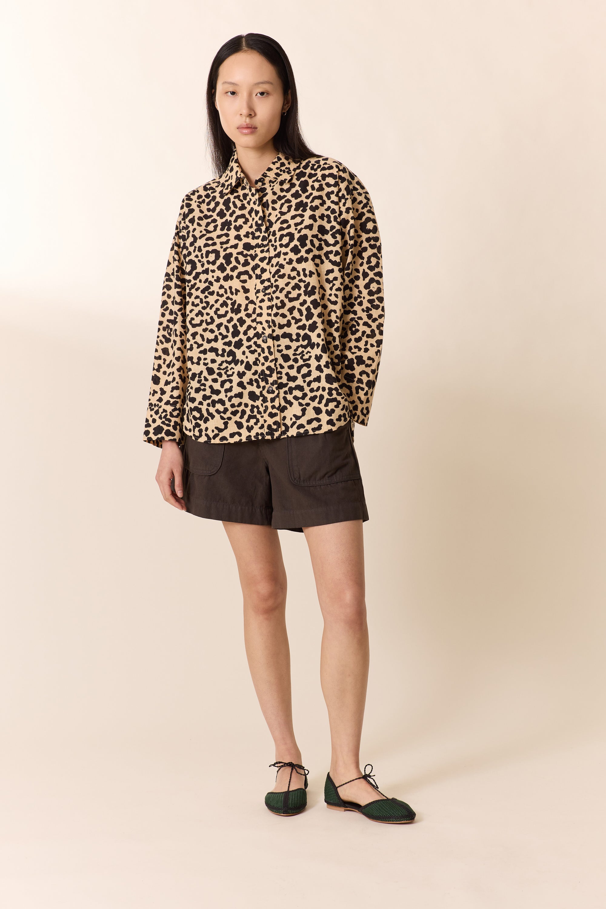 Woman wearing a leopard print  shirt with brown shorts on a plain studio background. 