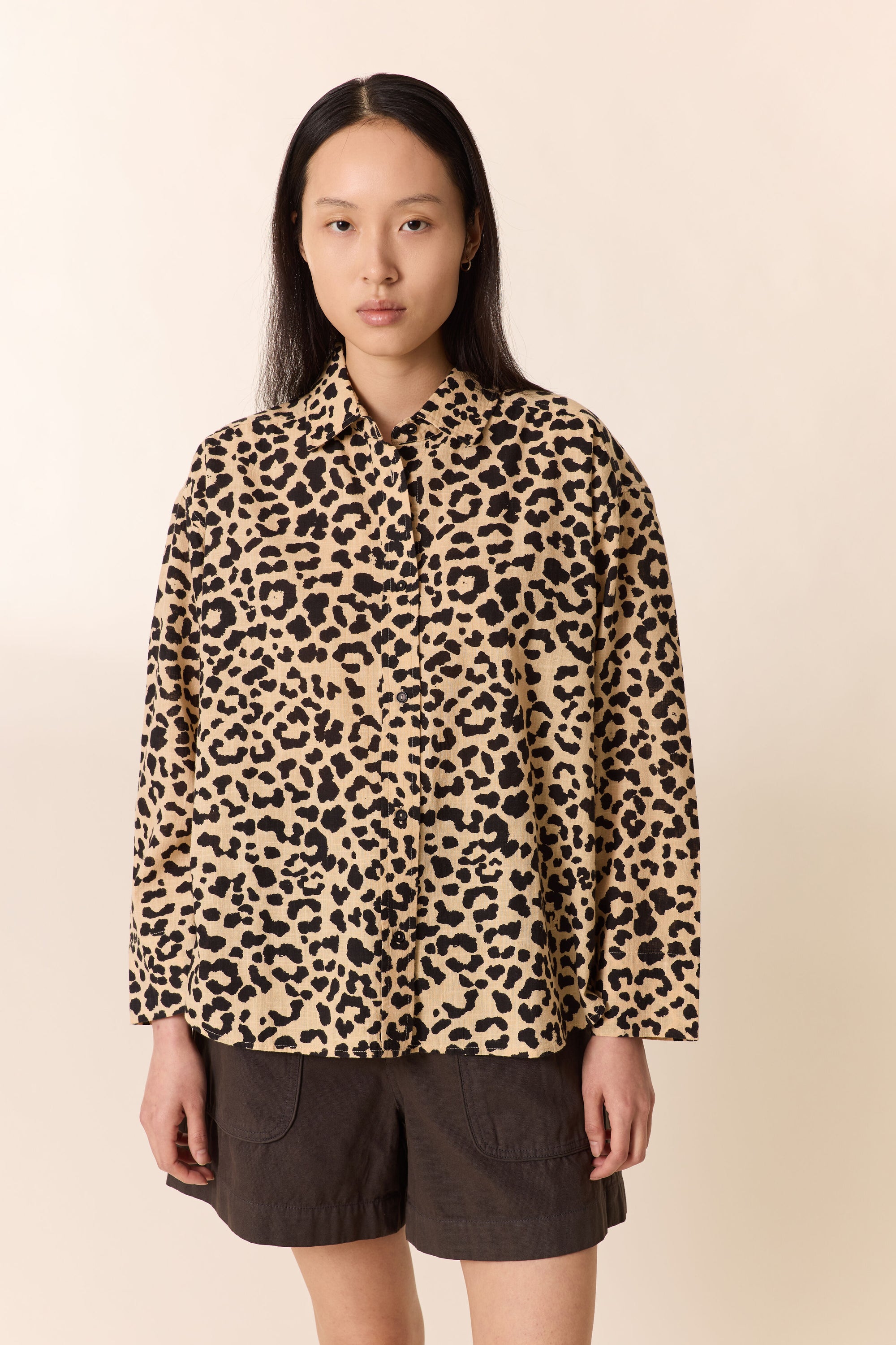 Woman wearing a leopard print  shirt with brown shorts on a plain studio background. 